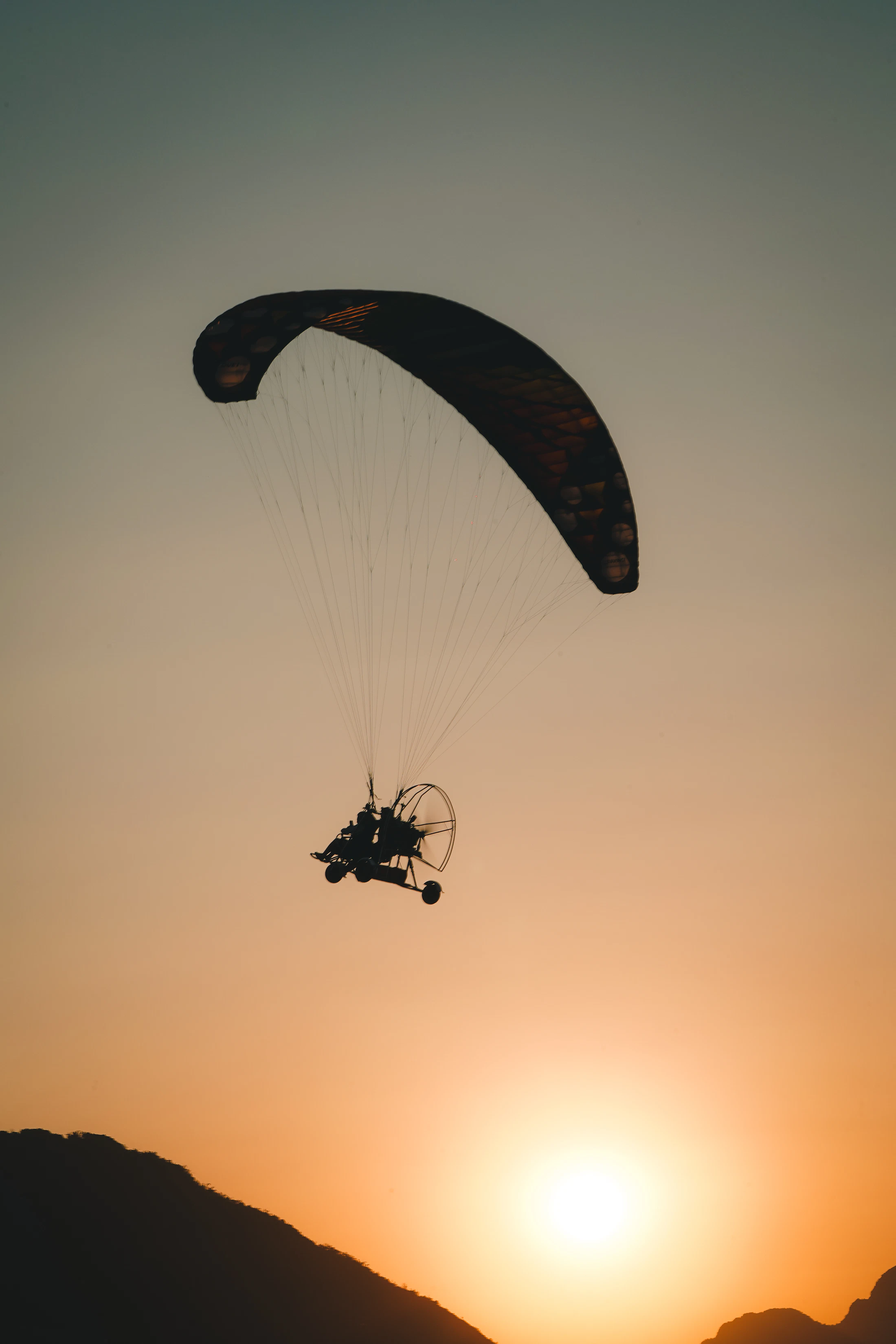 Paramotor silhouette flying against a Laos sunset