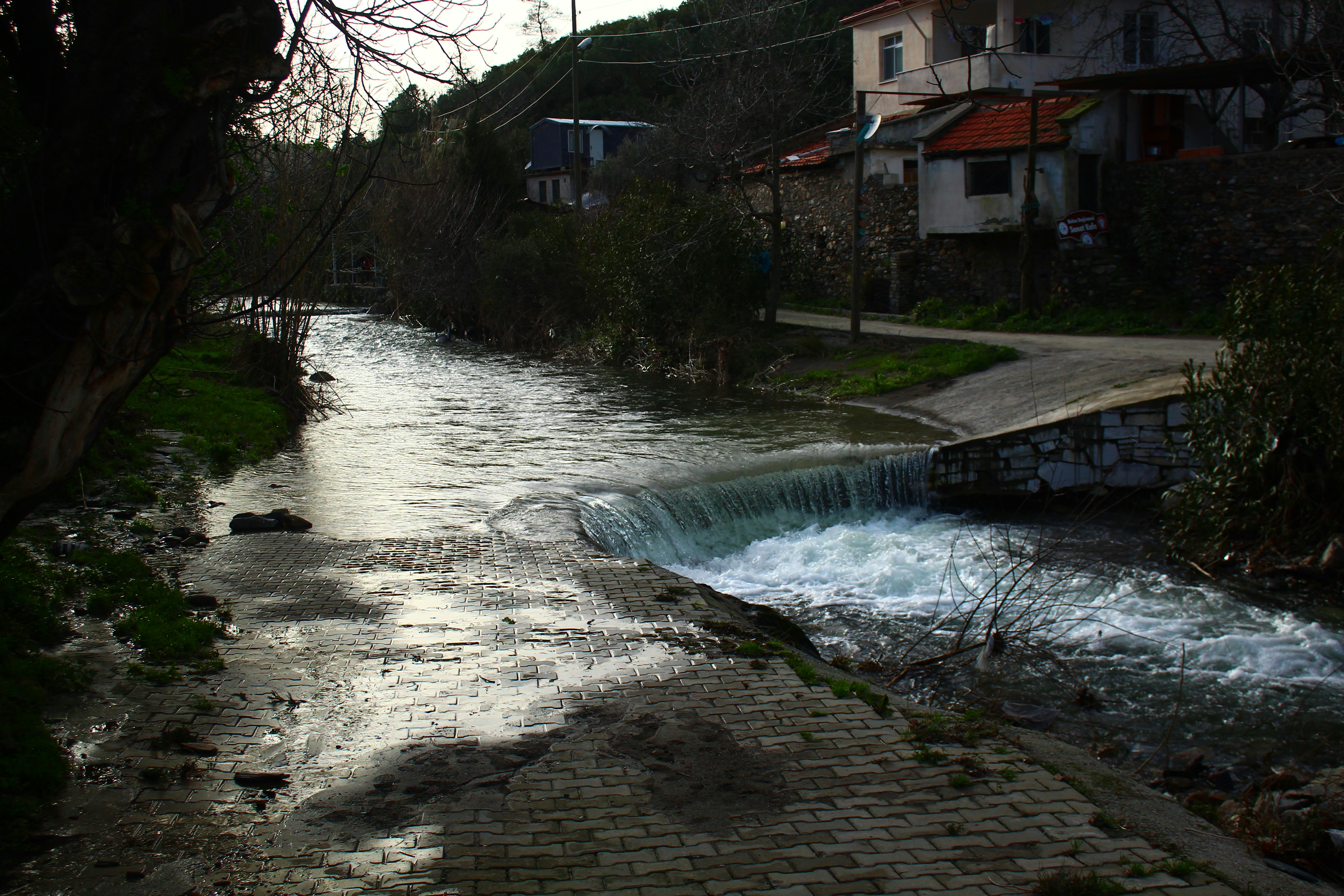 A small waterfall on a river near buildings.