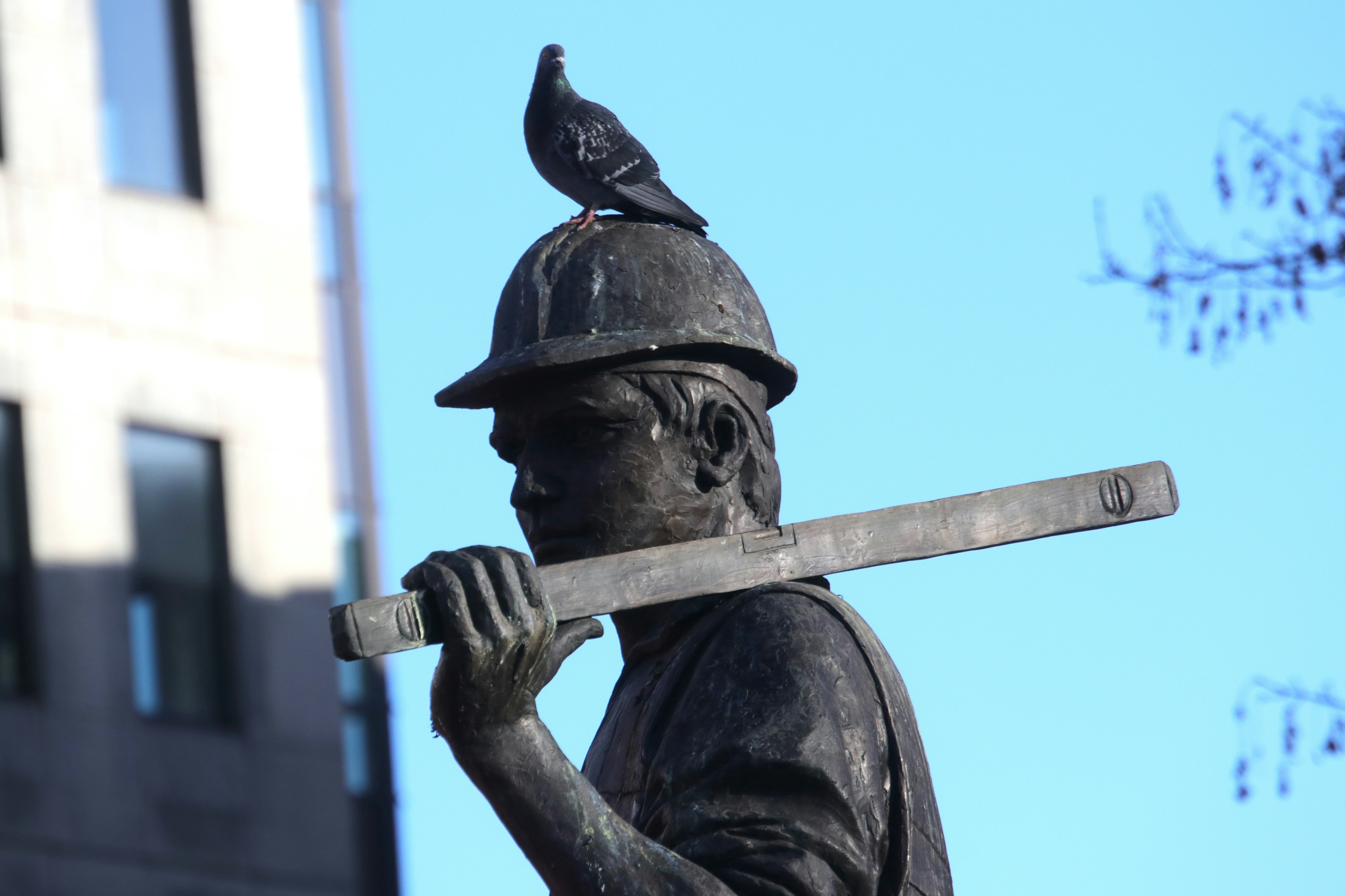 Pigeon rests on statue's hard hat carrying a level
