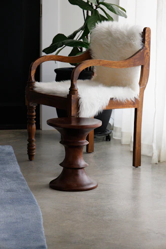 Wooden armchair with fluffy white seat cover and back cushions.