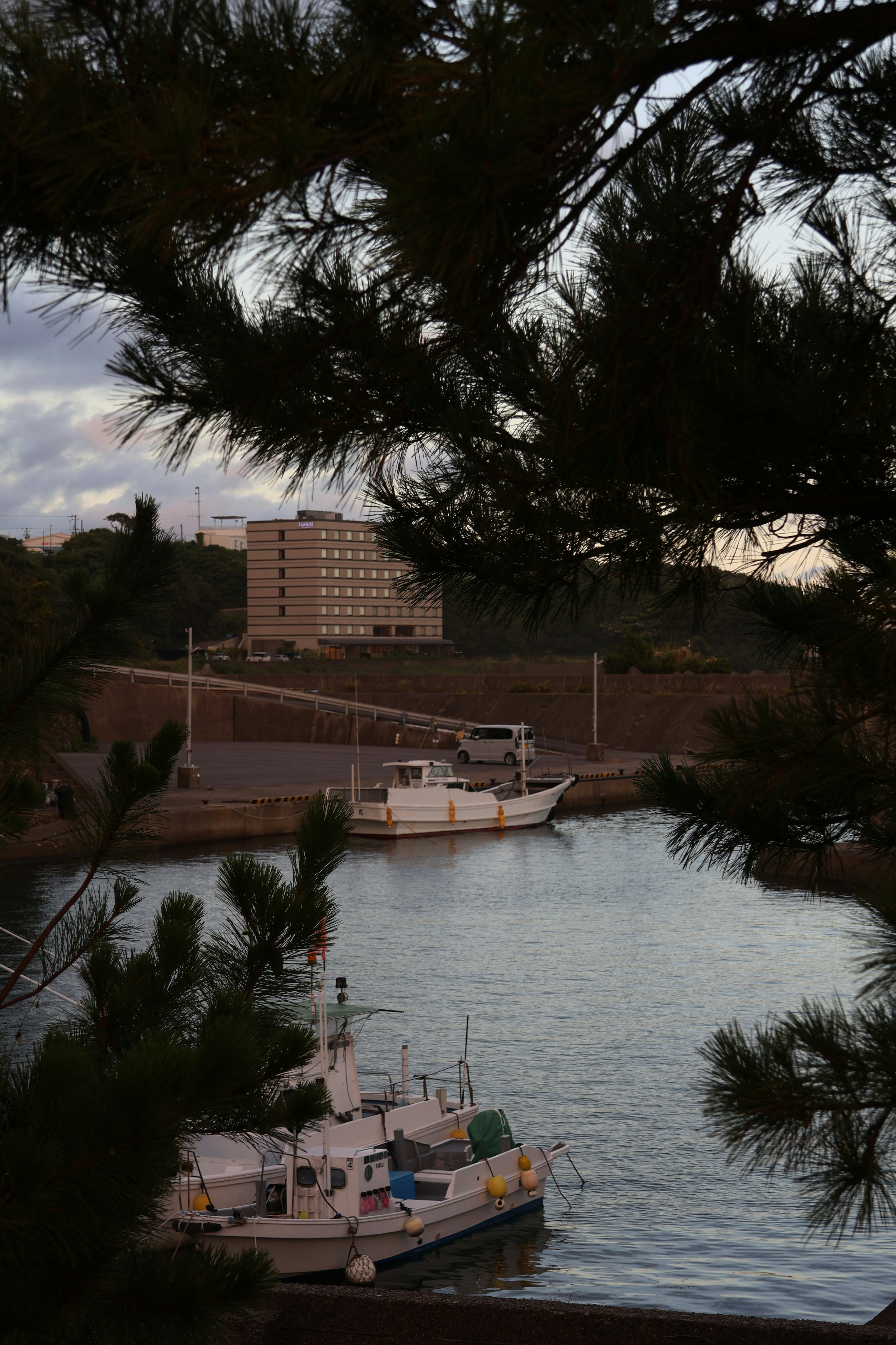 Two boats docked in a calm harbor with building background.