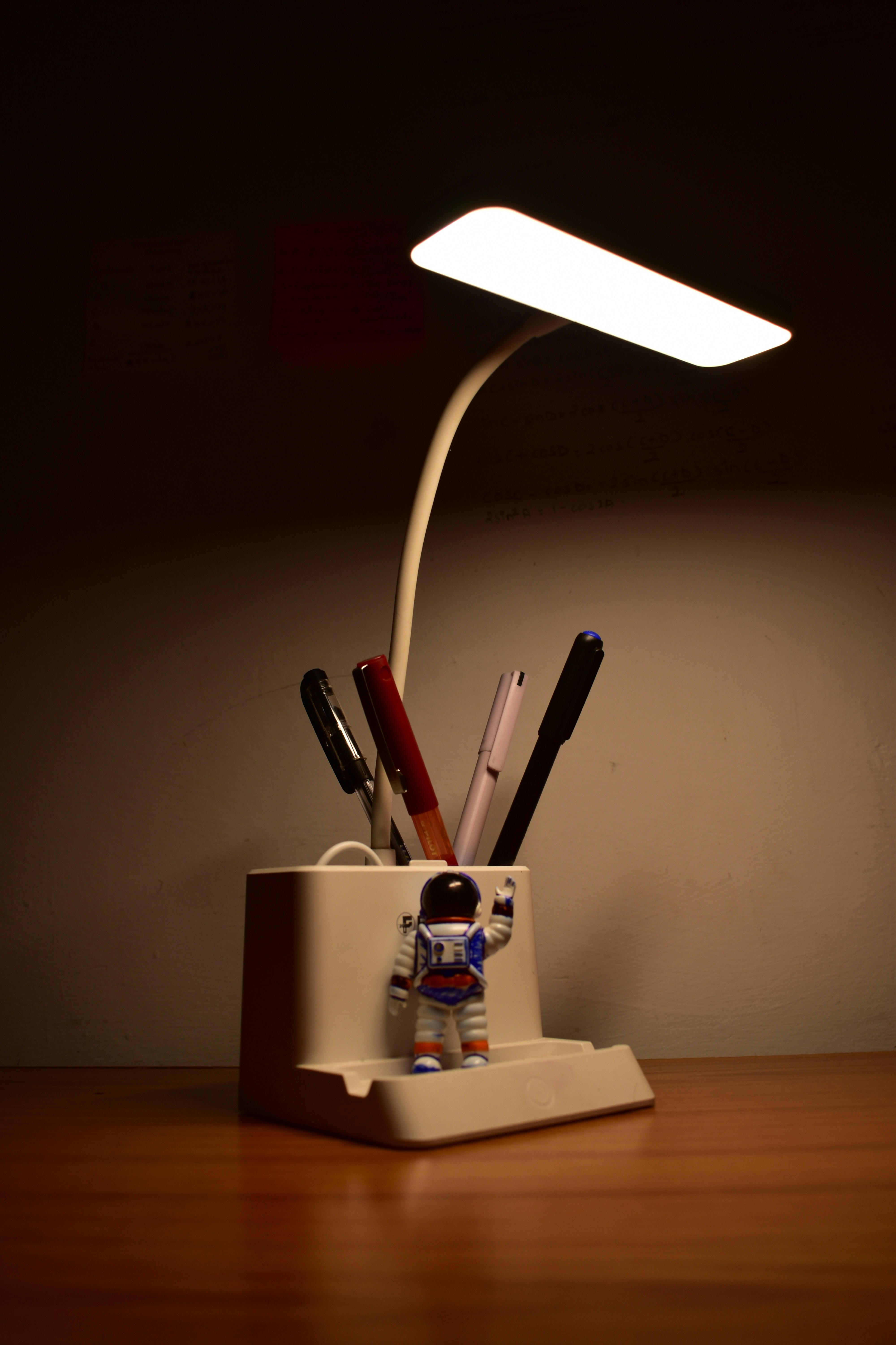 La lámpara de escritorio ilumina la figurita de astronauta y los bolígrafos en el portafuerzas.