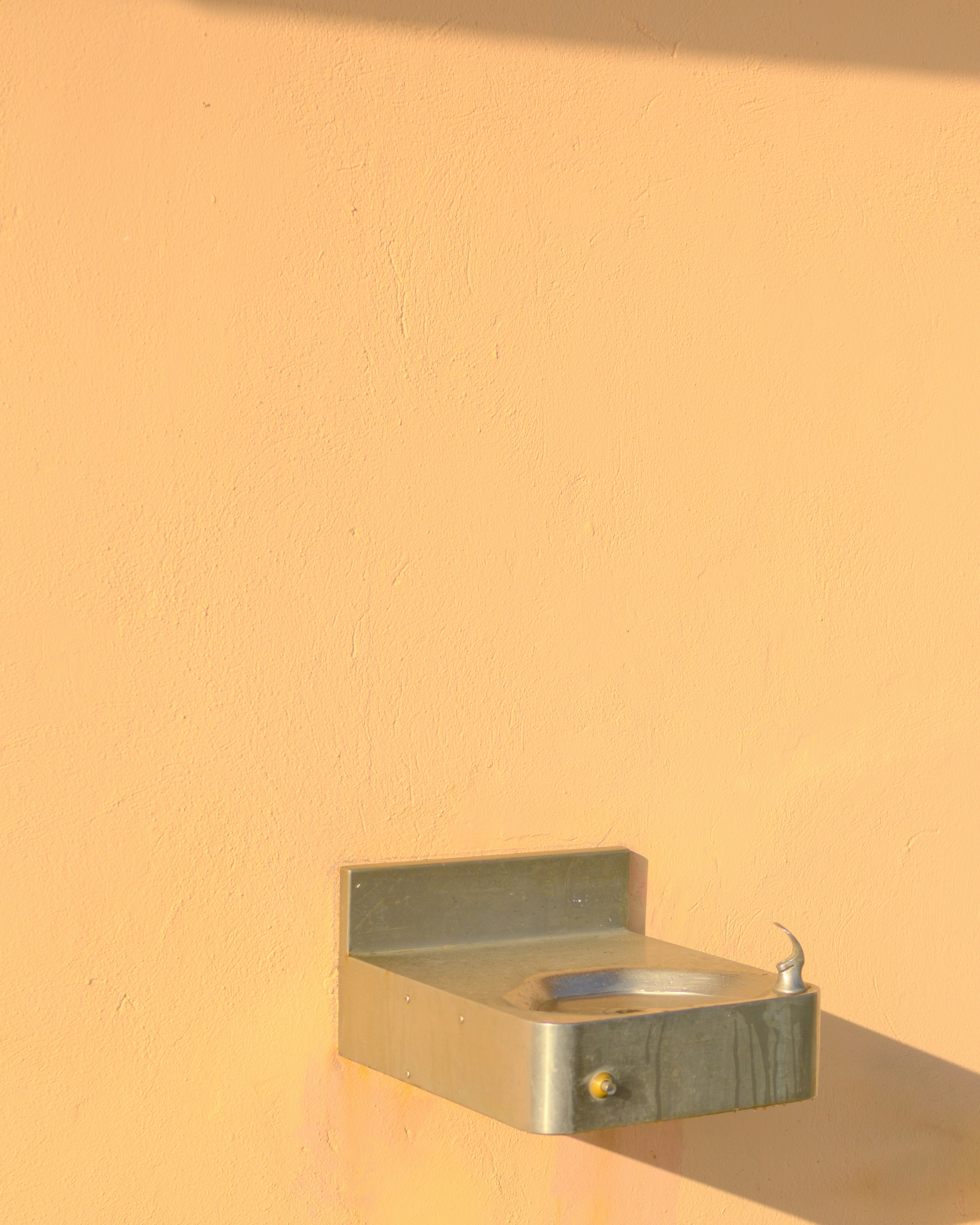 A metal drinking fountain mounted on a peach wall.