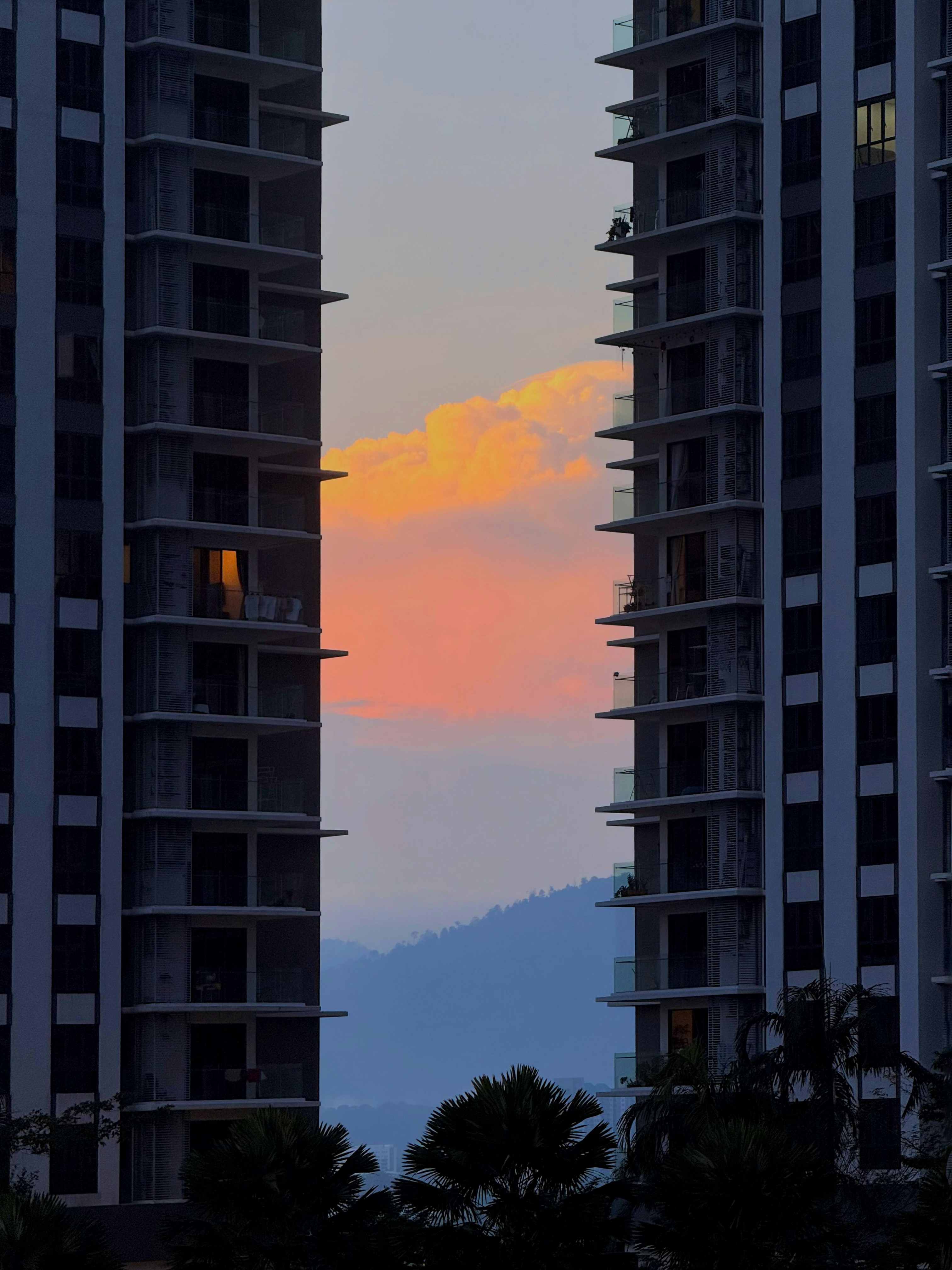 Two buildings frame a vibrant sunset over mountains.