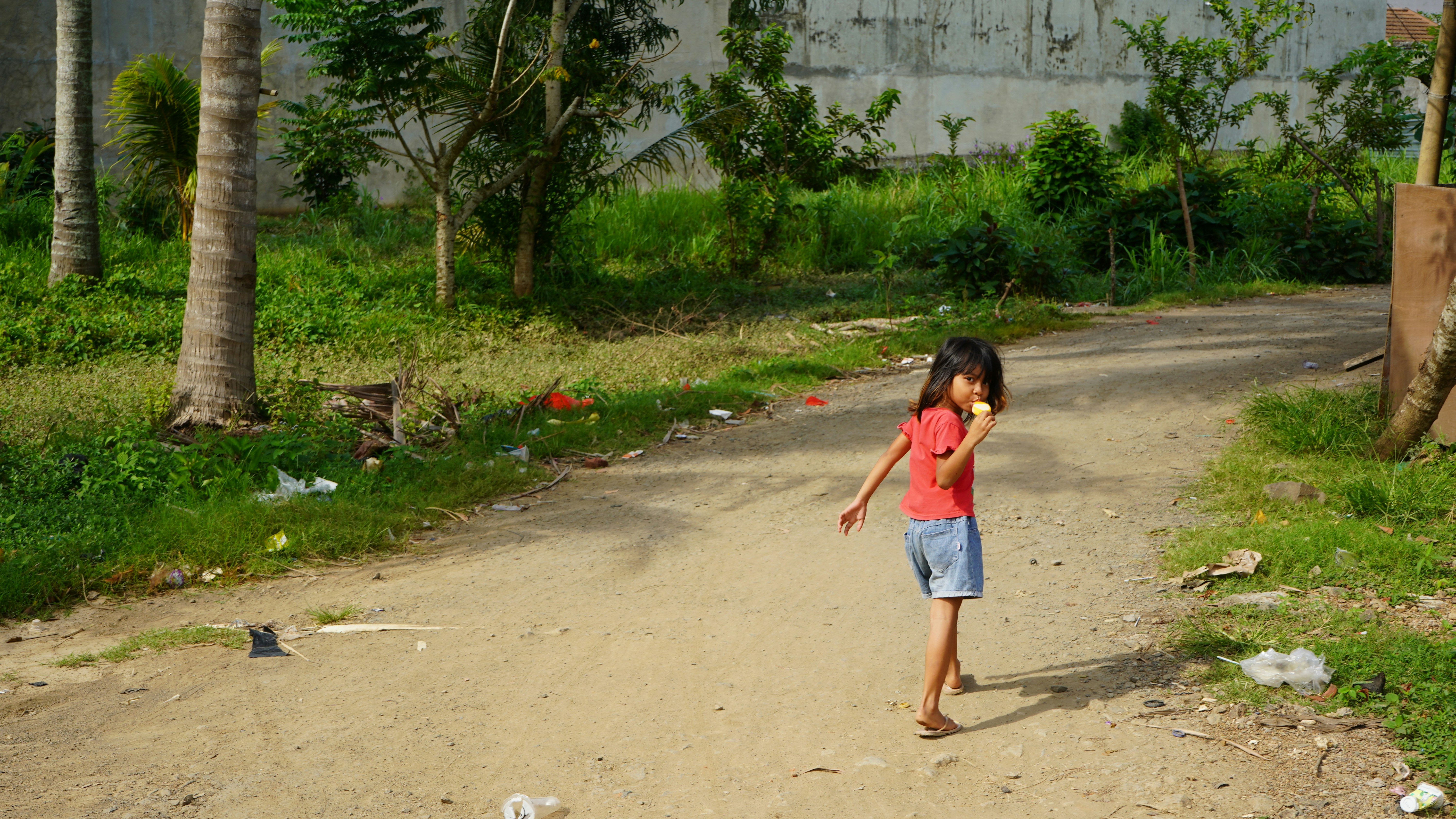 A young girl stands on a dirt road.
