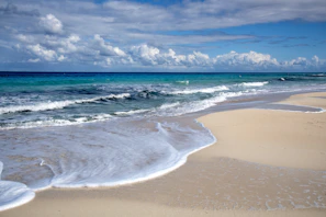 Waves gently lap onto a sandy beach under blue skies.