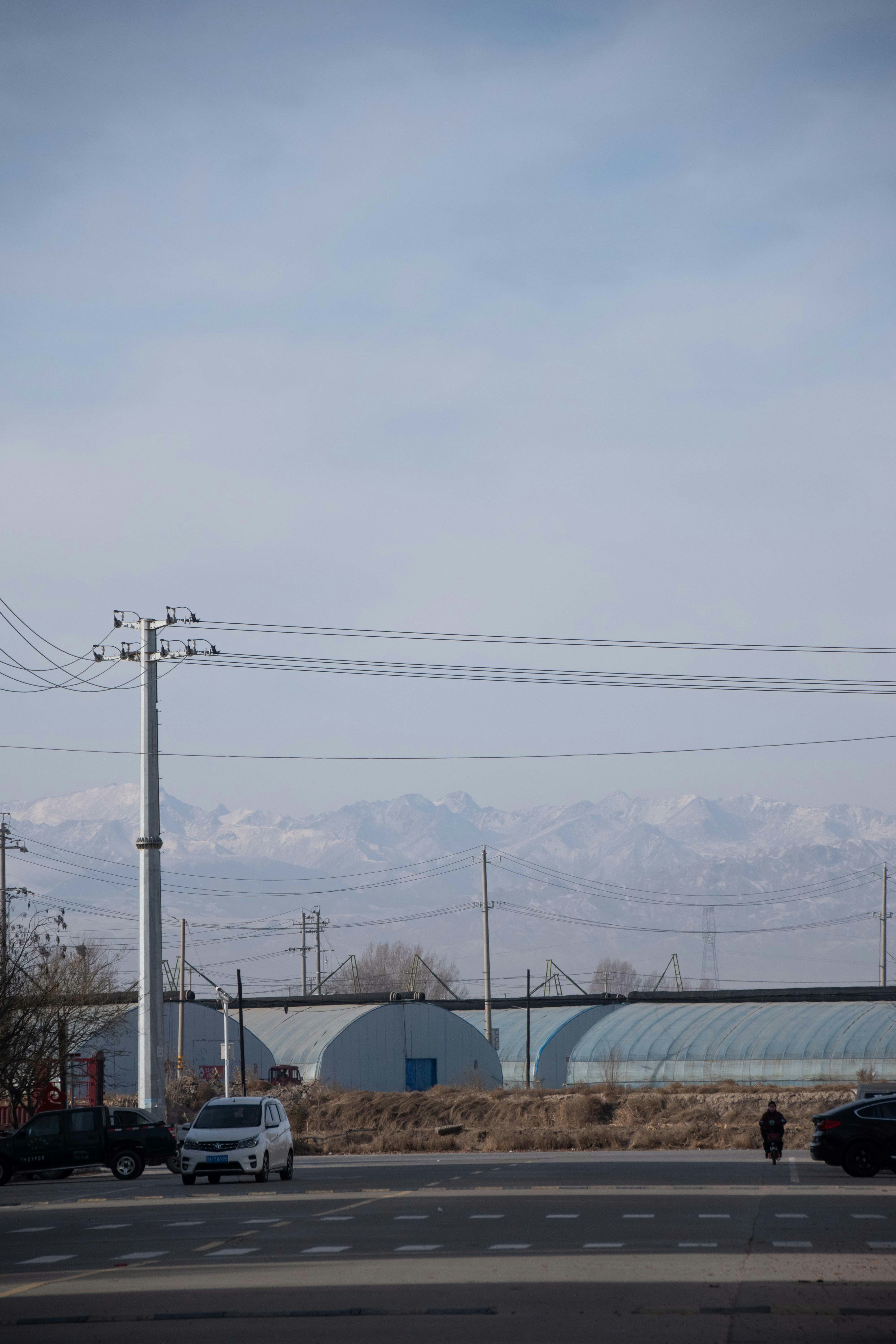 Cars on road with industrial buildings and mountains beyond.