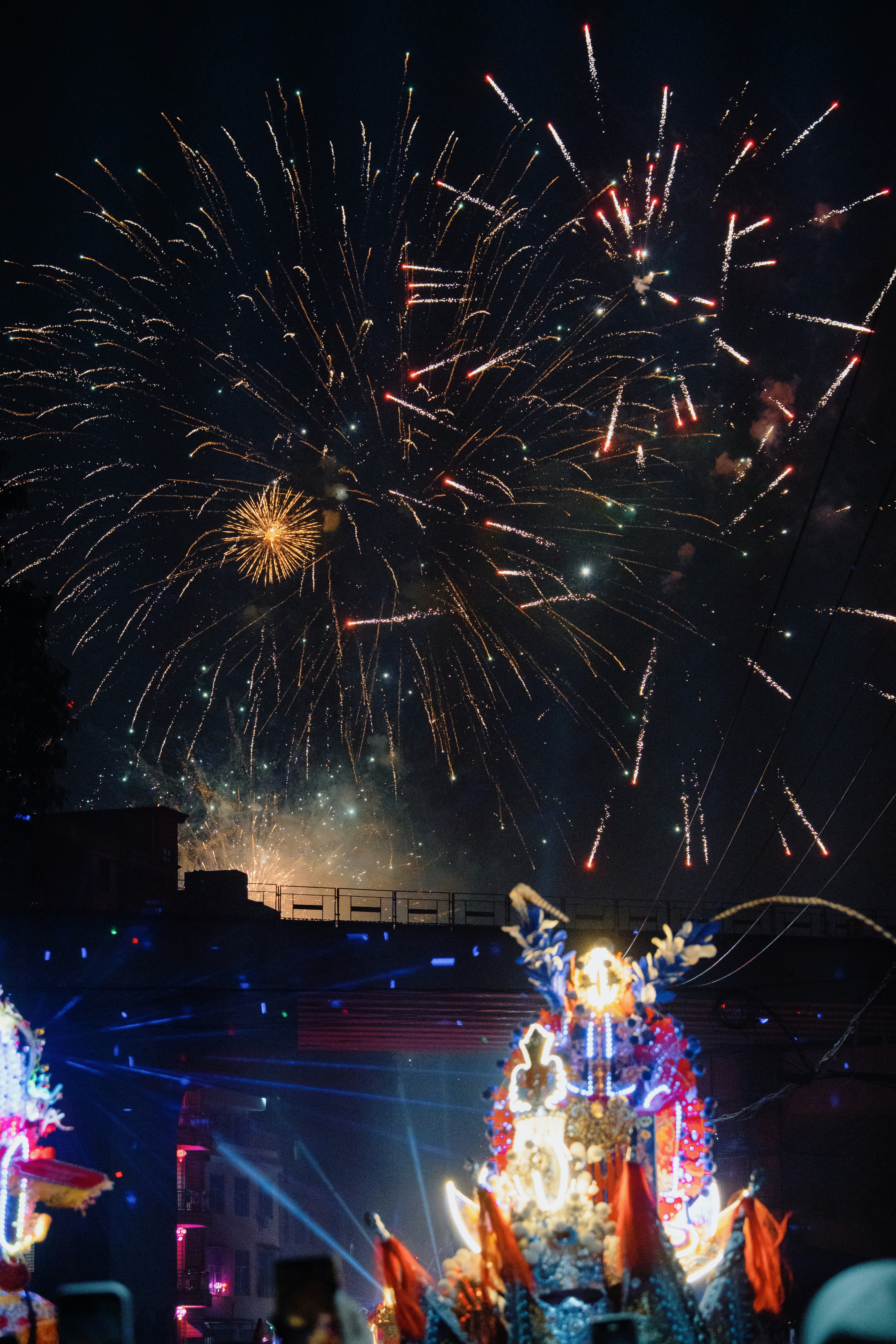 Des feux d’artifice colorés explosent au-dessus d’un char décoré la nuit.