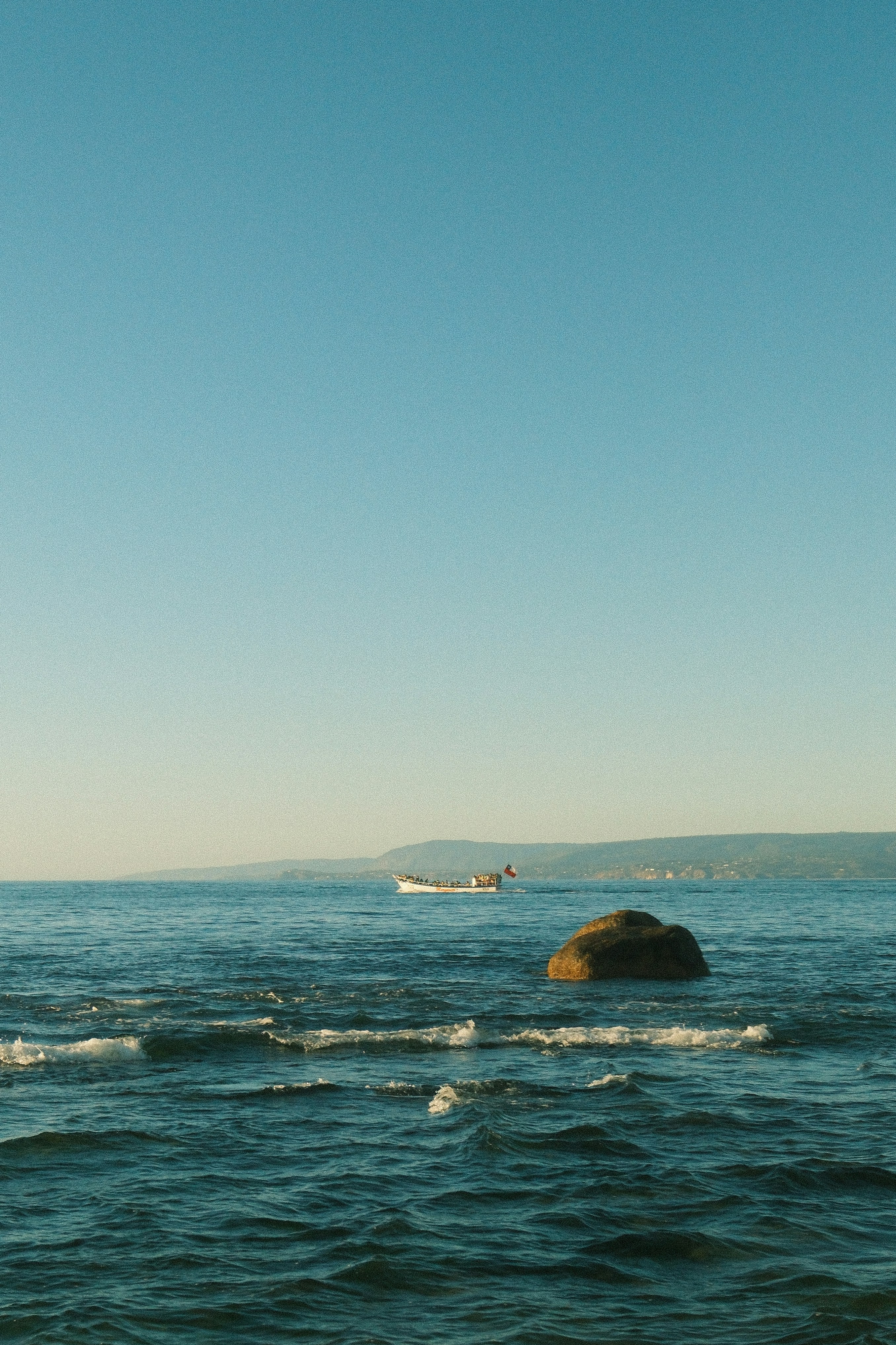 Ein ruhiges Meer mit einem entfernten Boot und einem großen Felsen.