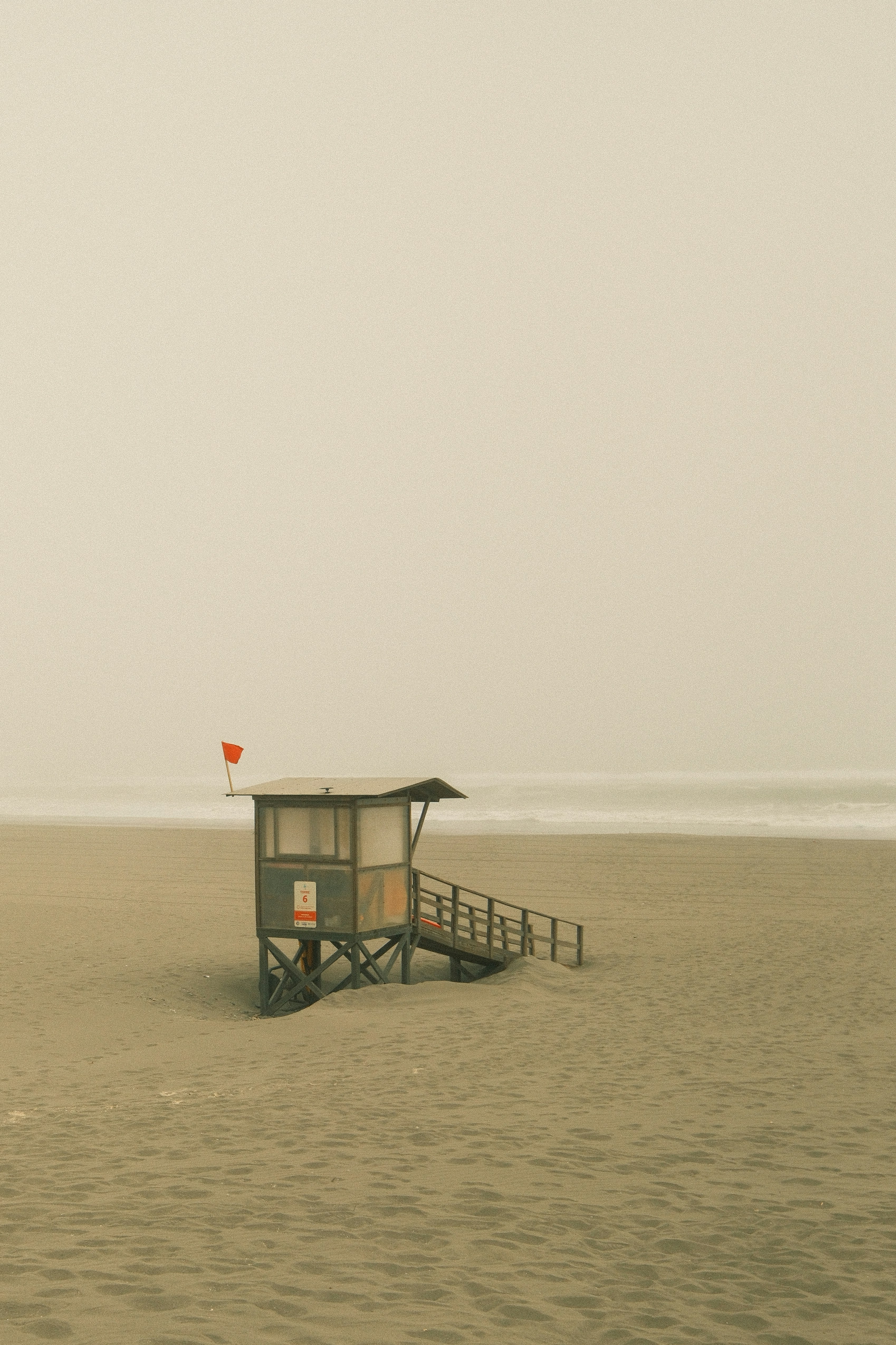 Rettungsschwimmerturm an einem nebligen Strand mit Meereswellen.