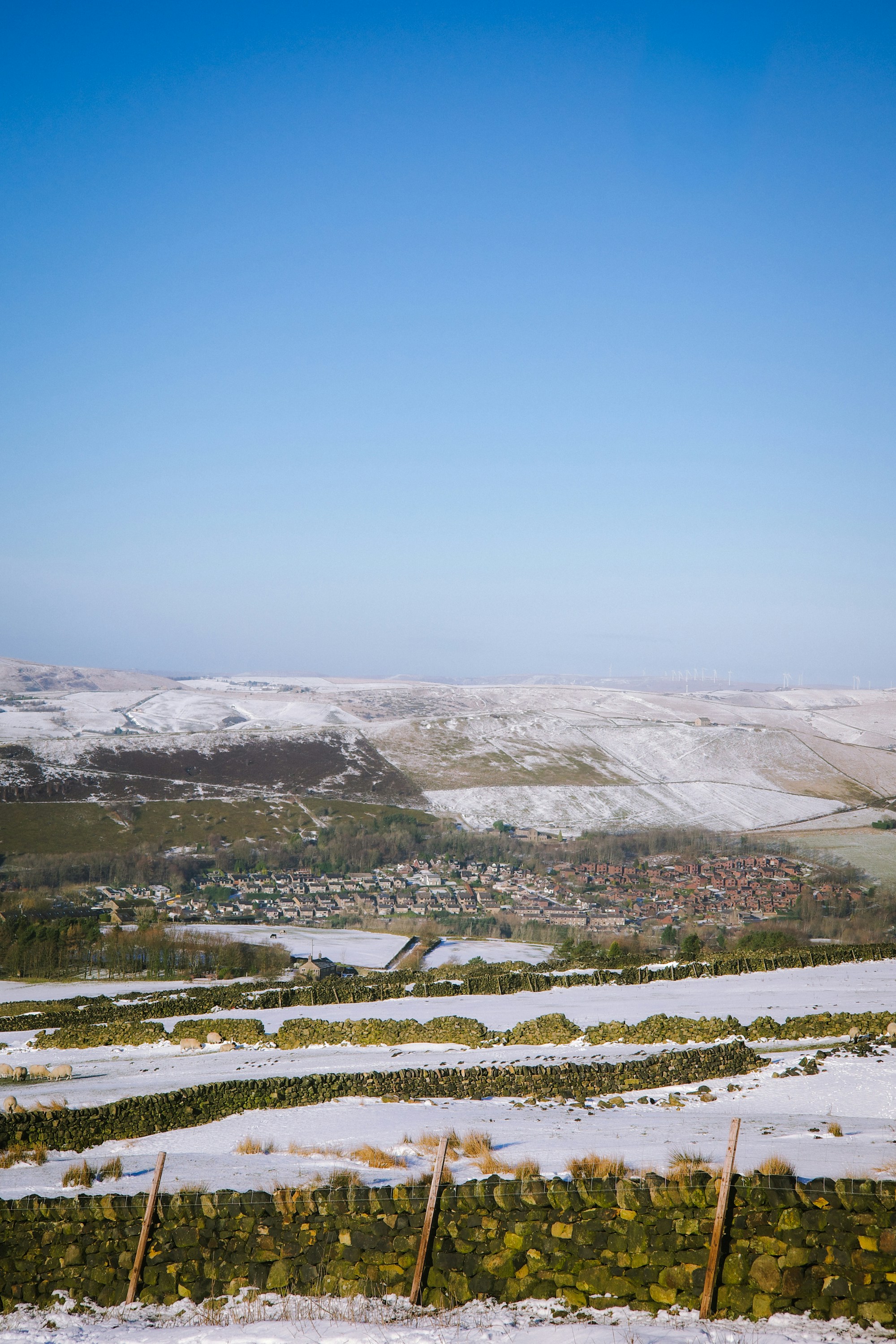 Snow-covered hills overlook a village under a clear blue sky.