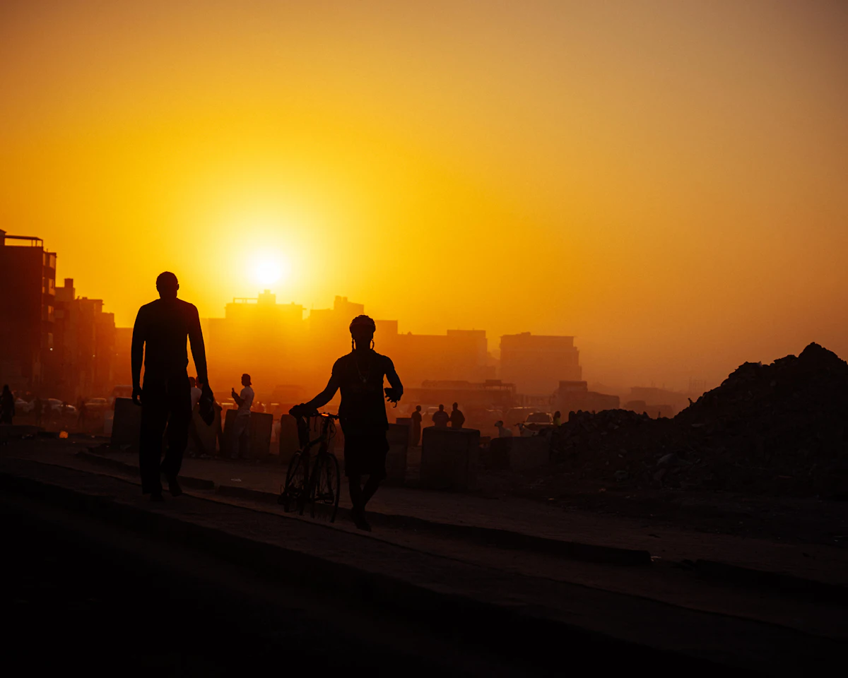 Silhouettes de passants au coucher du soleil devant des immeubles, à Dakar