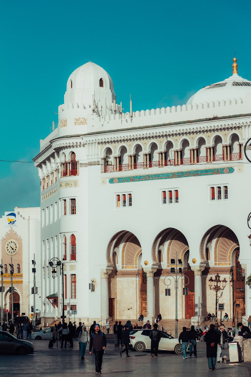 People walking in front of ornate white building with arches in Algeria