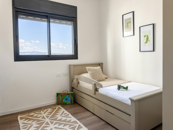Small child's bed with a built-in side guard rail and a single pillow in a bright, uncluttered bedroom