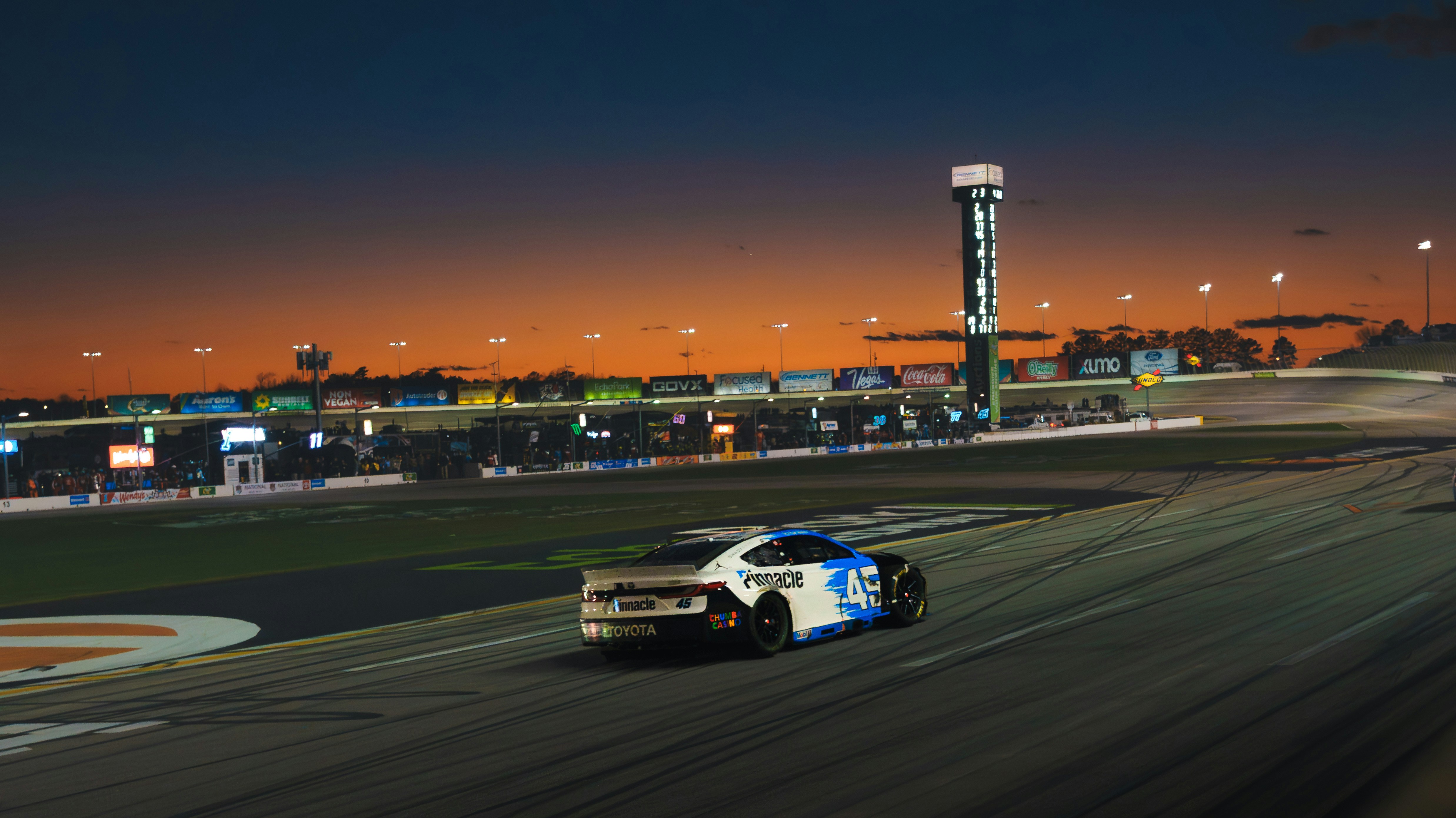 Race car on track at dusk with stadium lights.