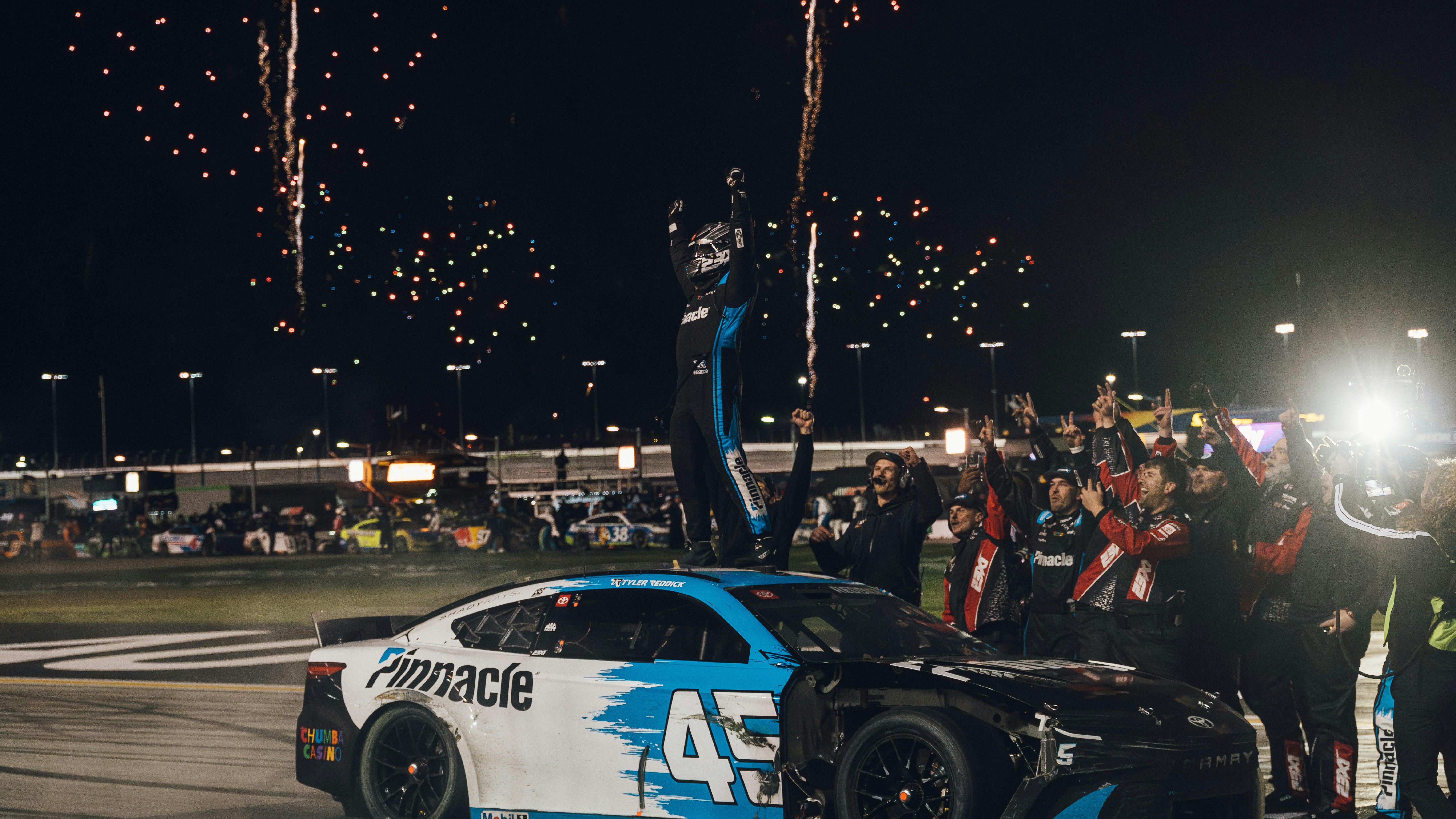 A race car driver stands on car with fireworks.