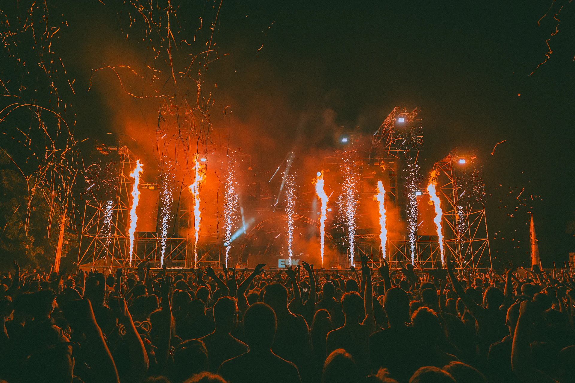 Fireworks erupt over a cheering crowd at a concert.