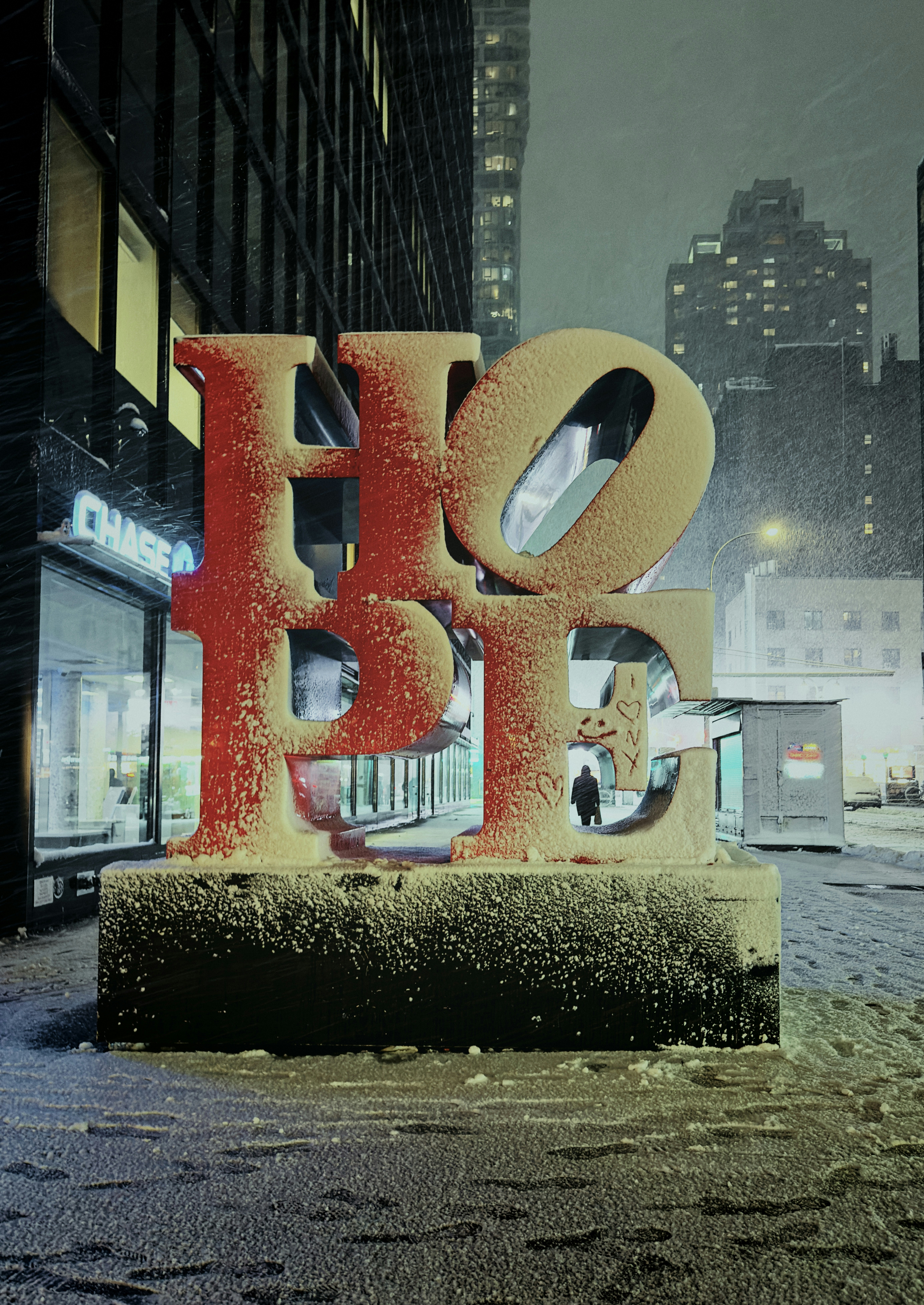 Large red hope sculpture covered in snow at night