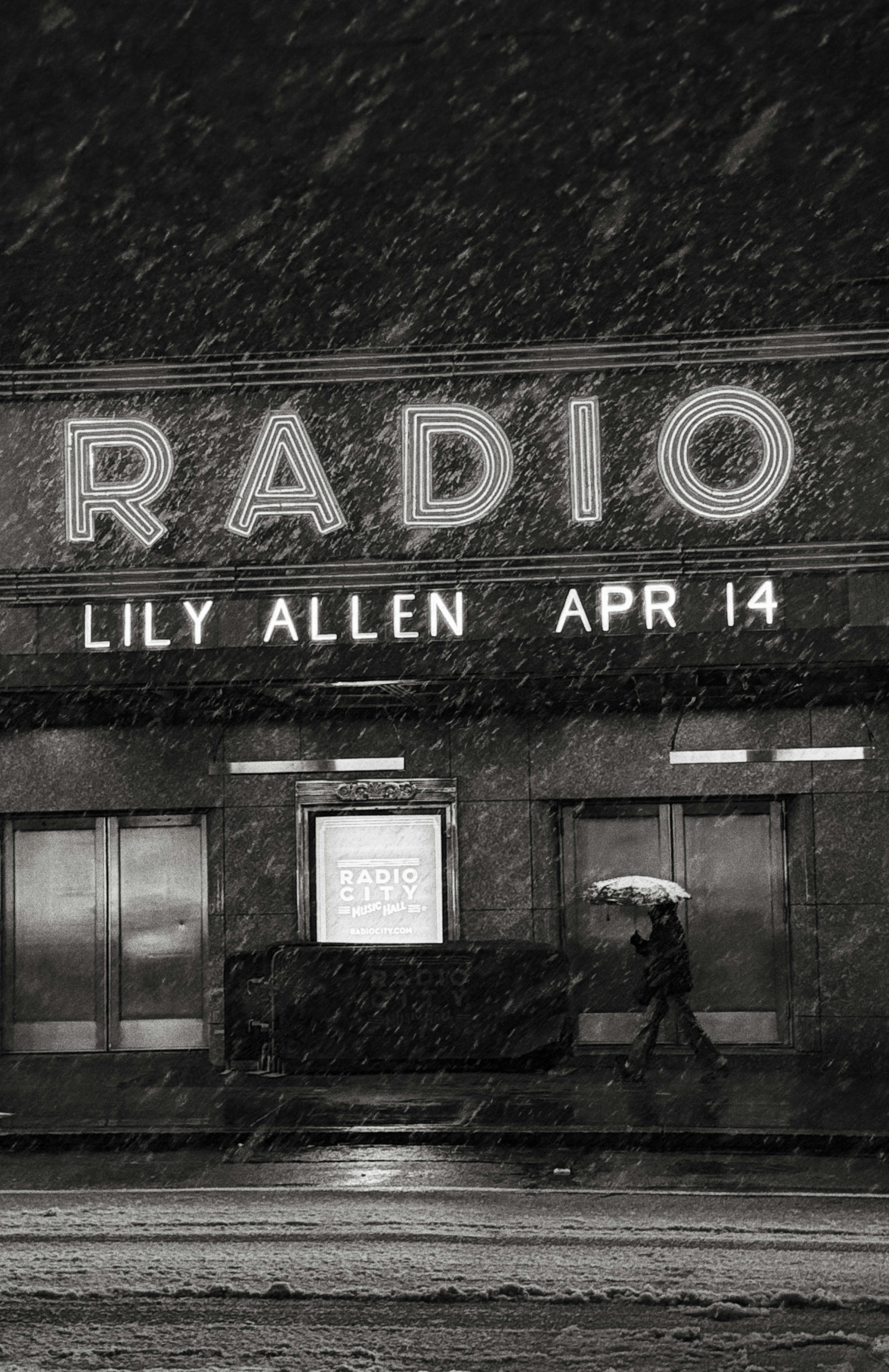 Person with umbrella walks past radio marquee in snow.