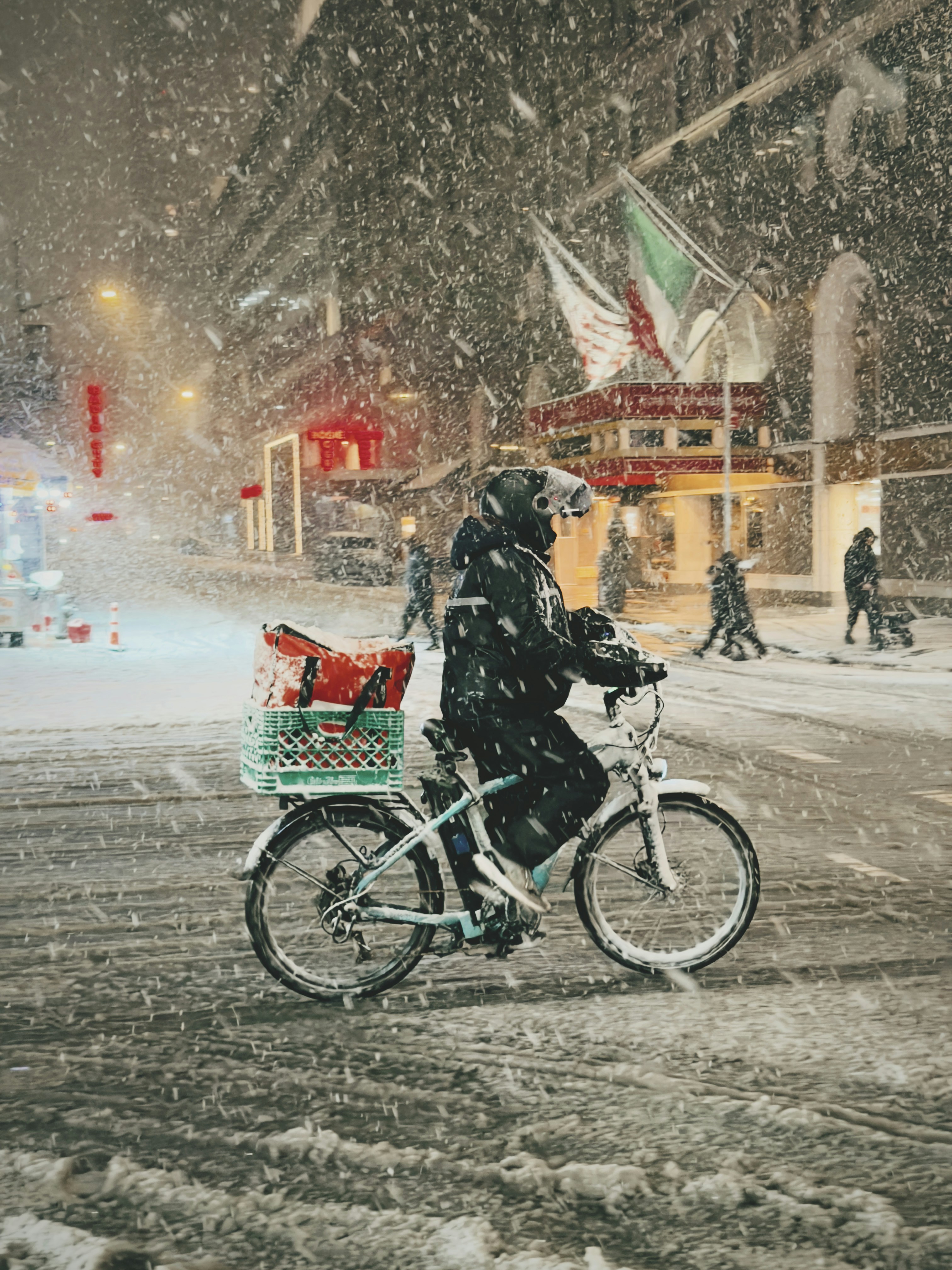 Person rides bicycle in heavy snowfall on city street.