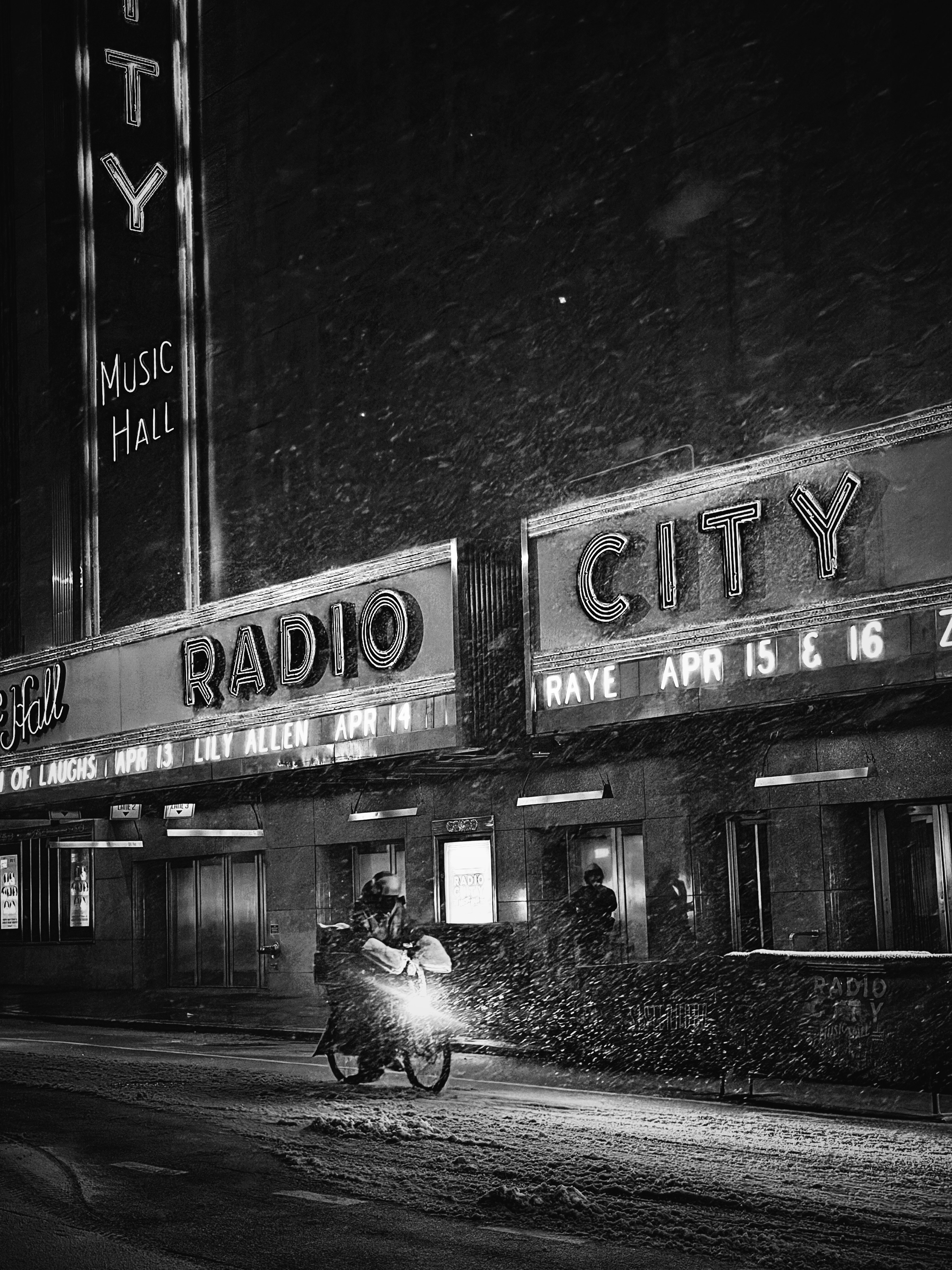 A motorcycle rider passes radio city music hall at night.