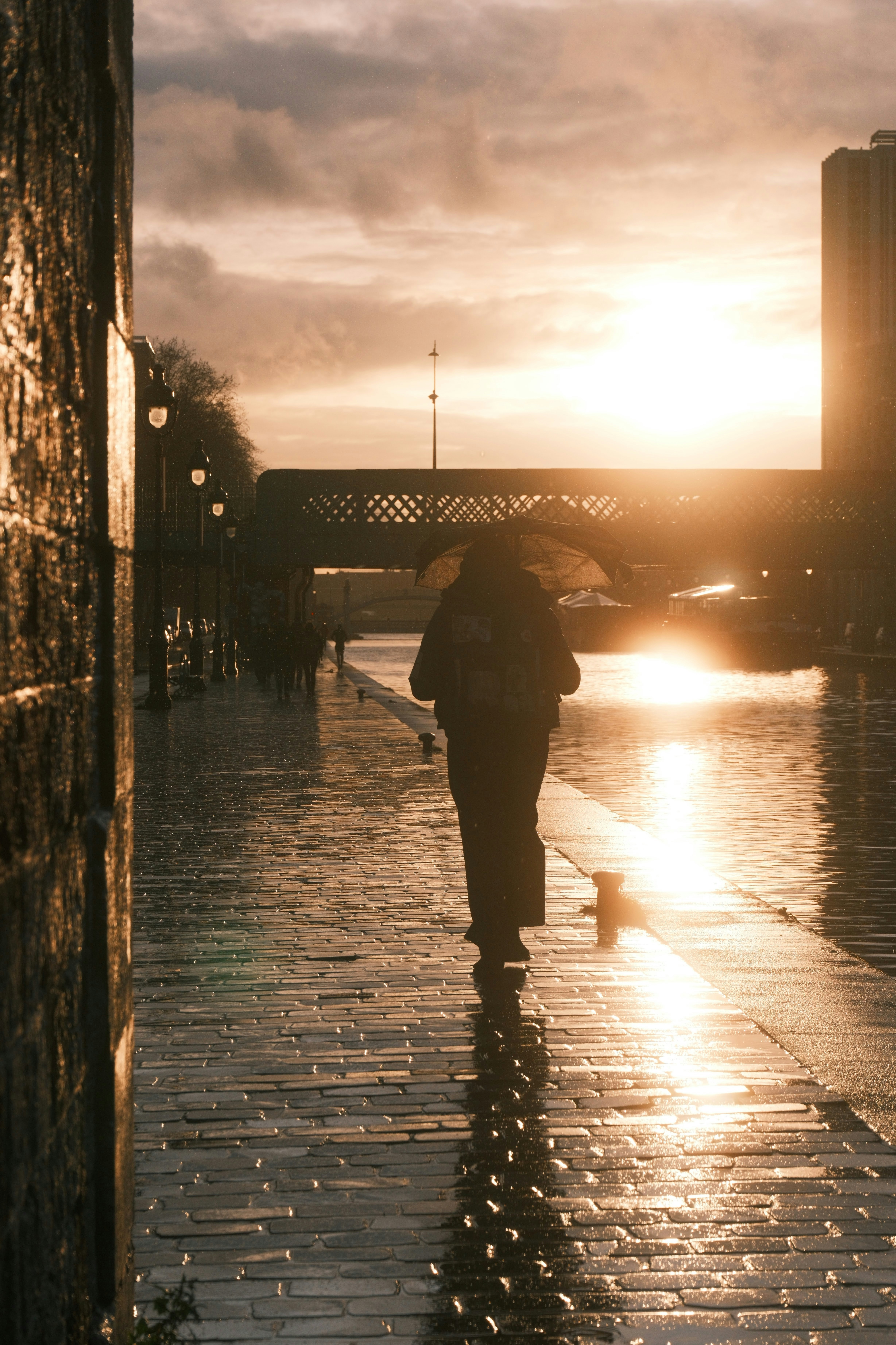 Person with umbrella walks by canal at sunset