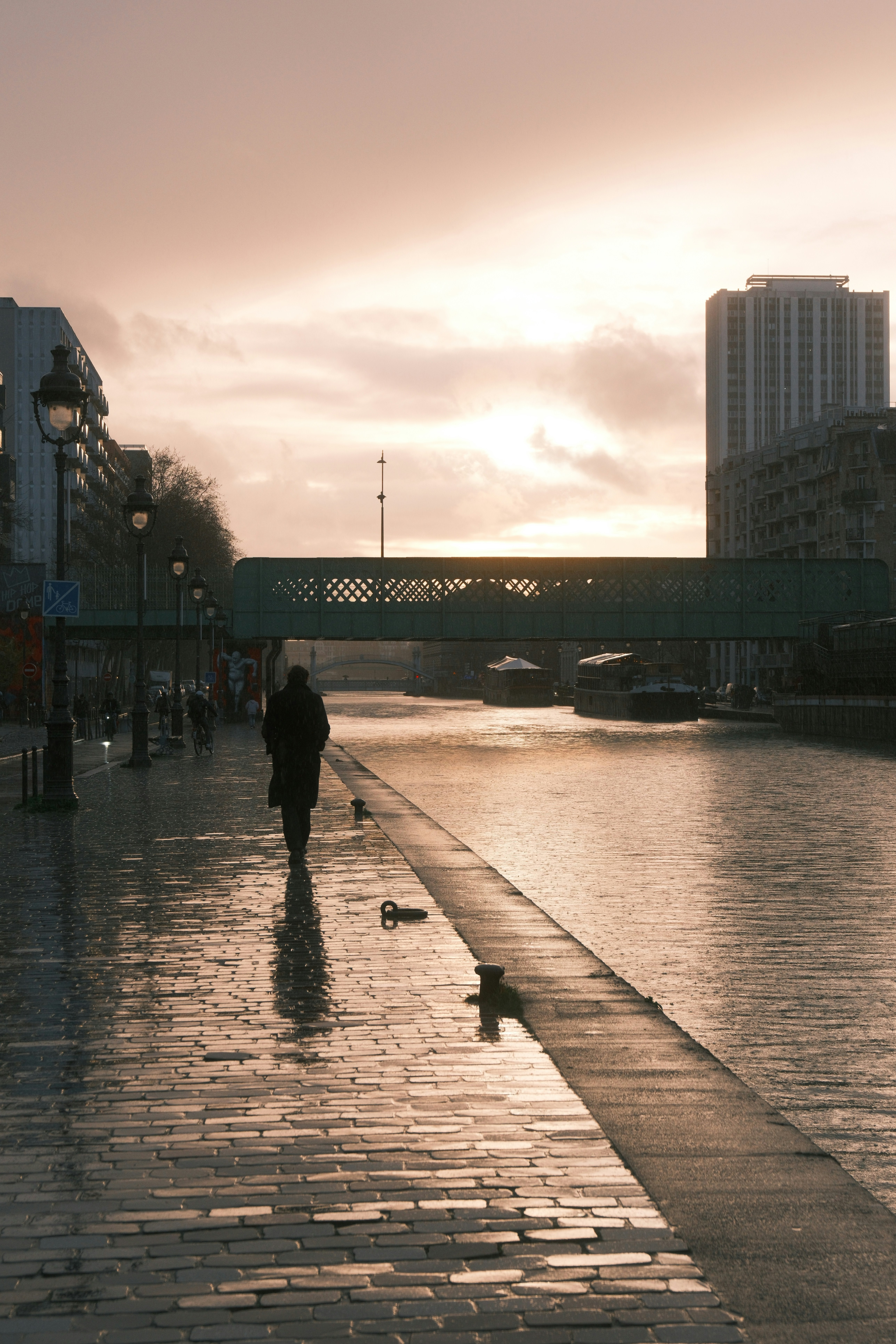 A person walks along a wet canal path at dusk.