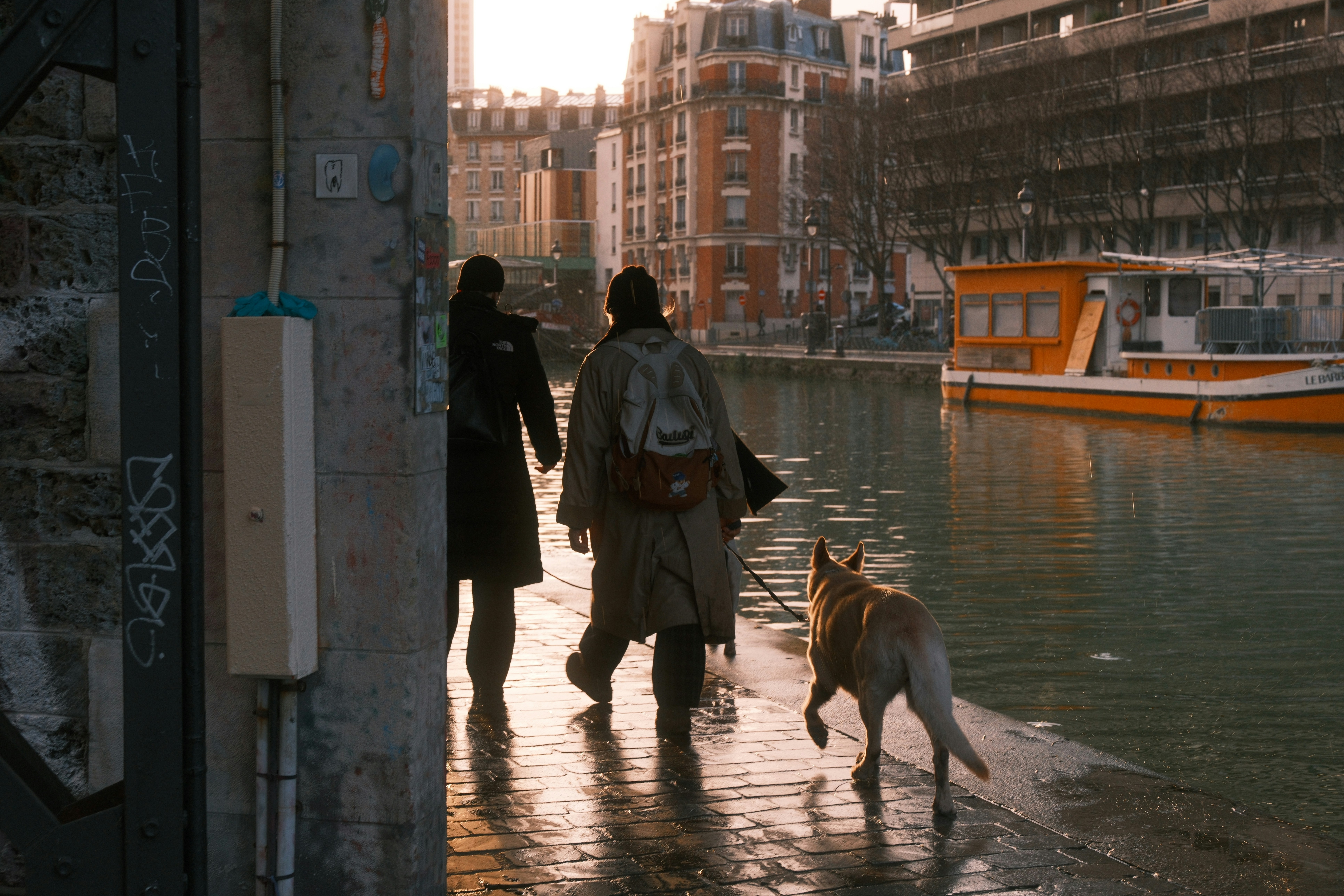 Two people and a dog walk along a canal.