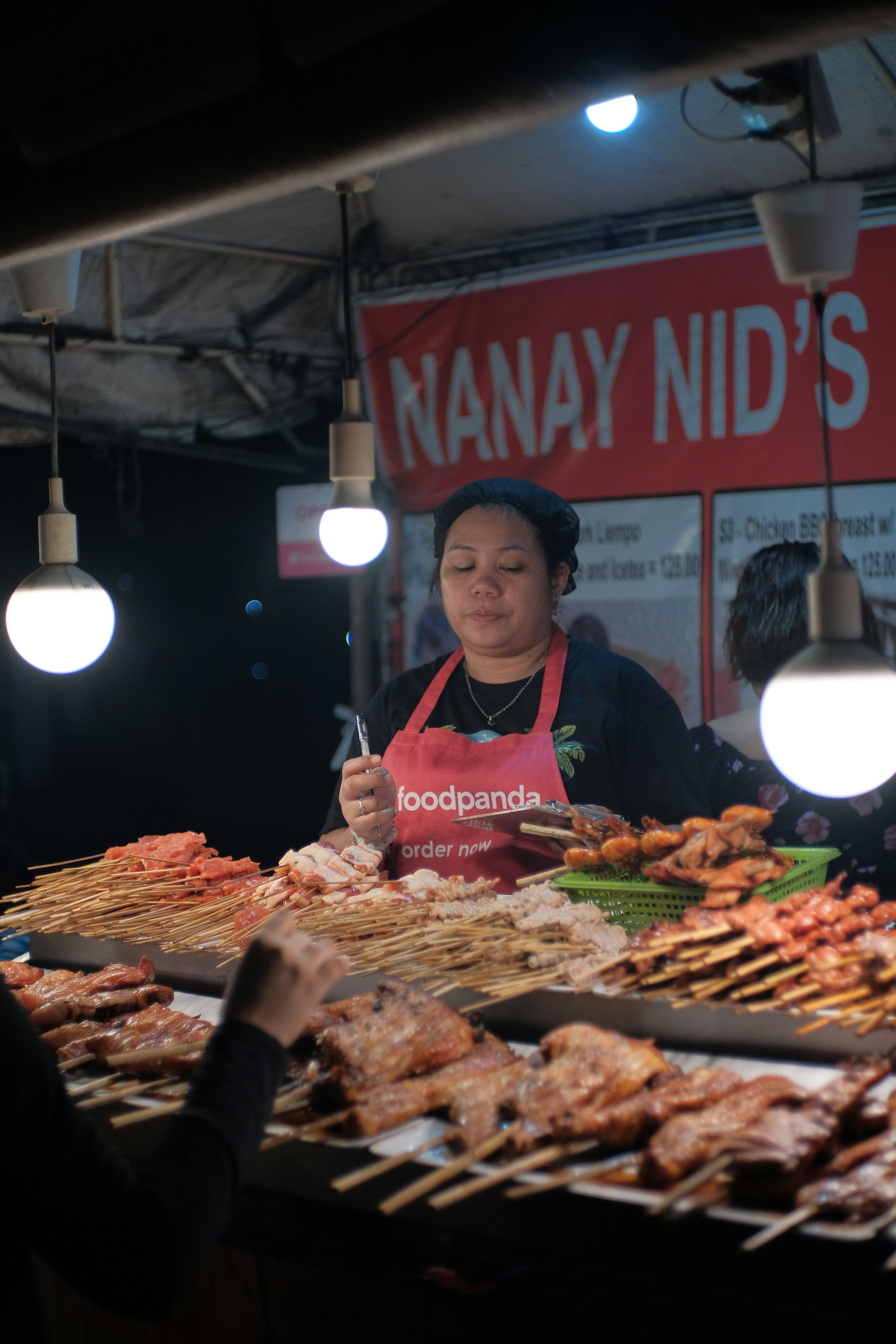 Woman serving skewers at a food stall at night