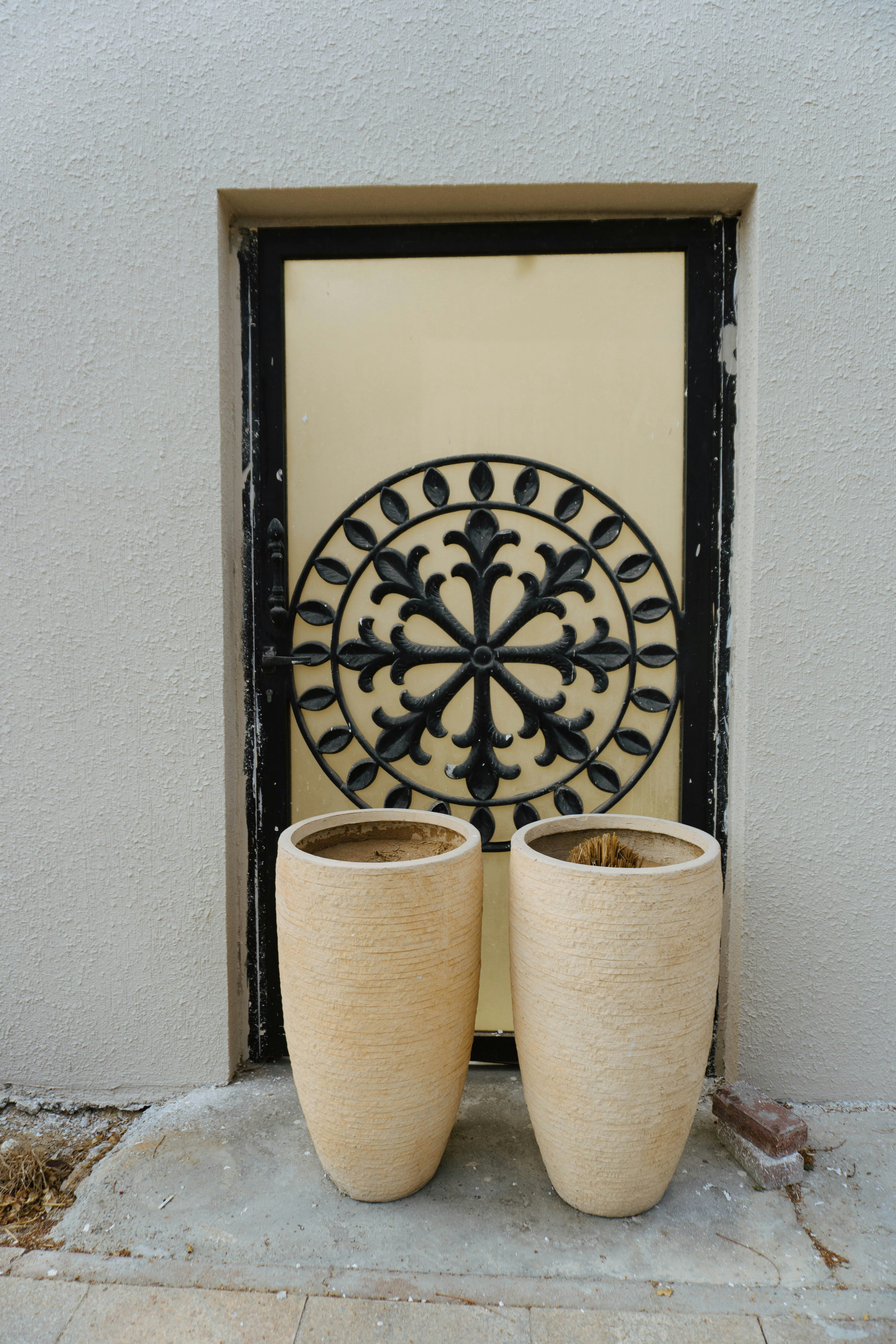 Zwei große Pflanzgefäße flankieren eine cremefarbene Tür mit kunstvollen Metallarbeiten.