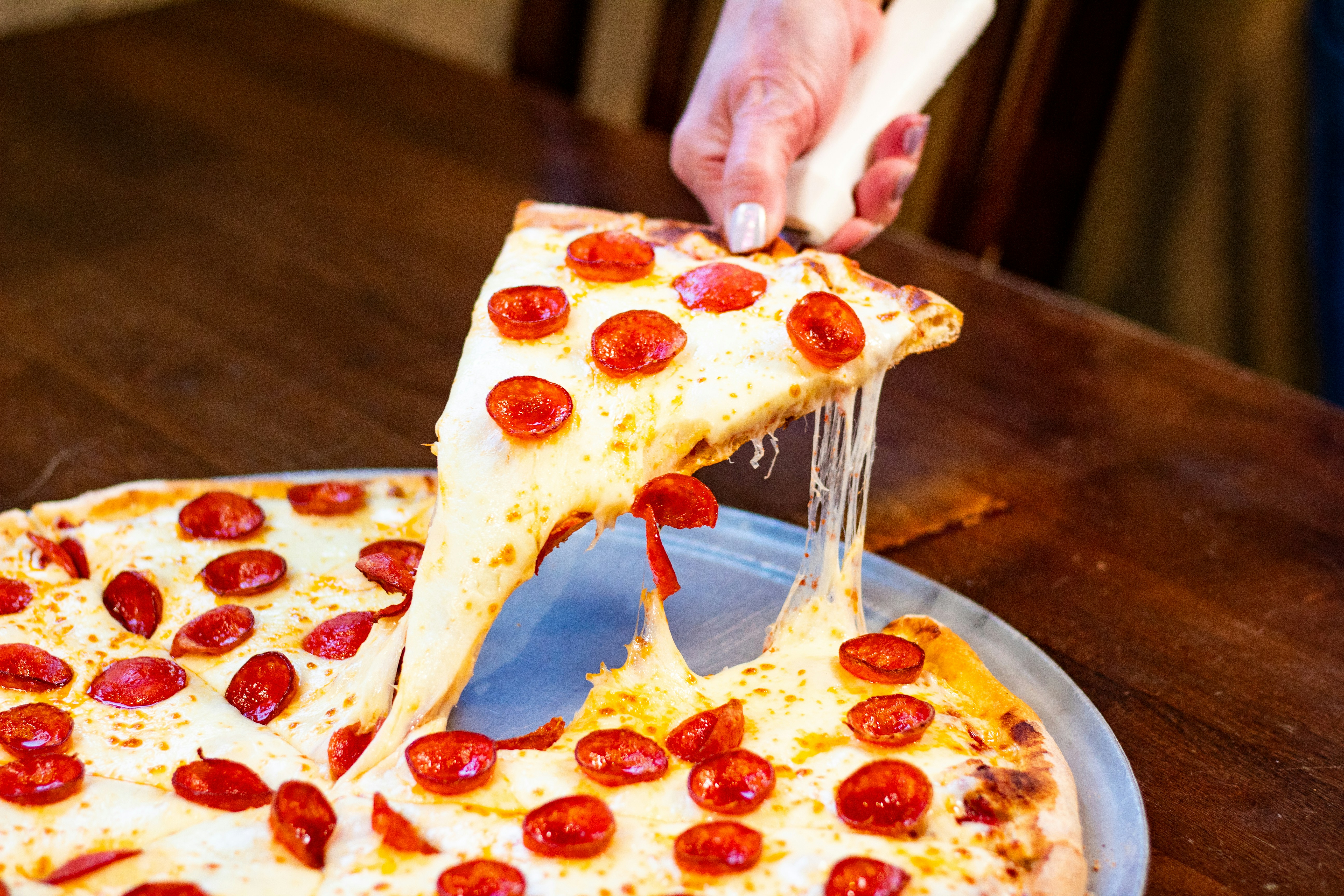 A hand lifts a cheesy slice of pepperoni pizza.