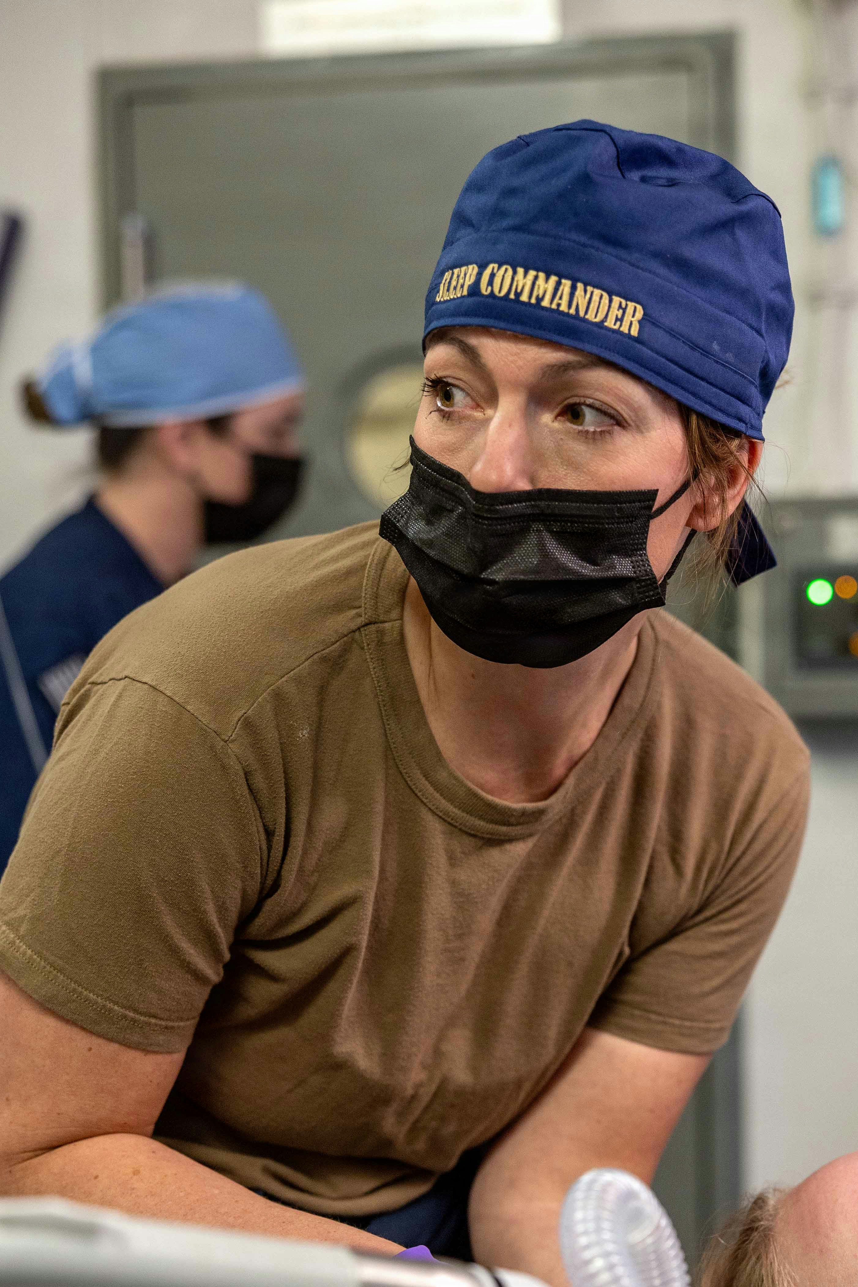 Mulher de jaleco médico e touca cirúrgica olha atentamente.