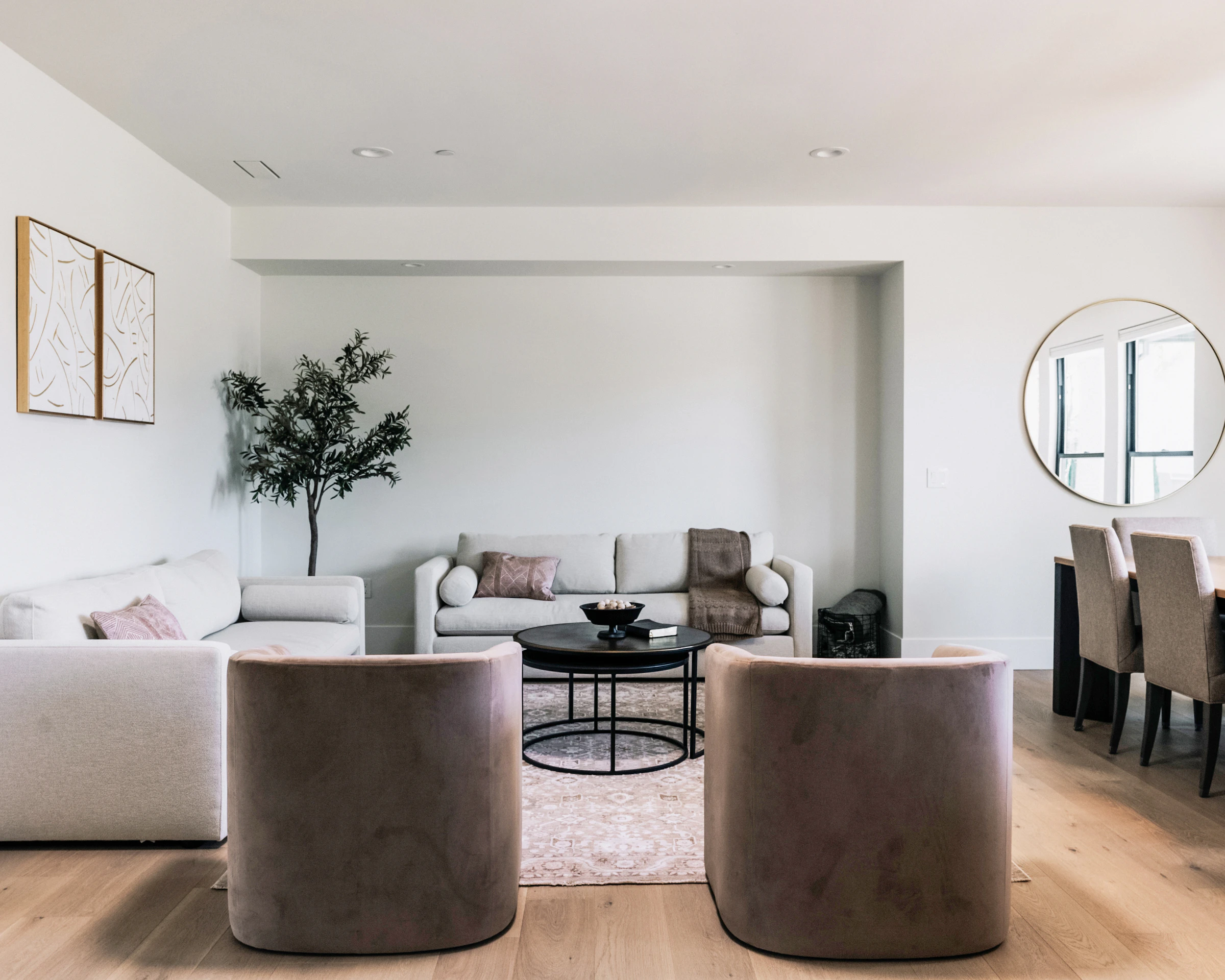 Warm modern living room with neutral sofas, accent chairs, a coffee table, rug, and wall art