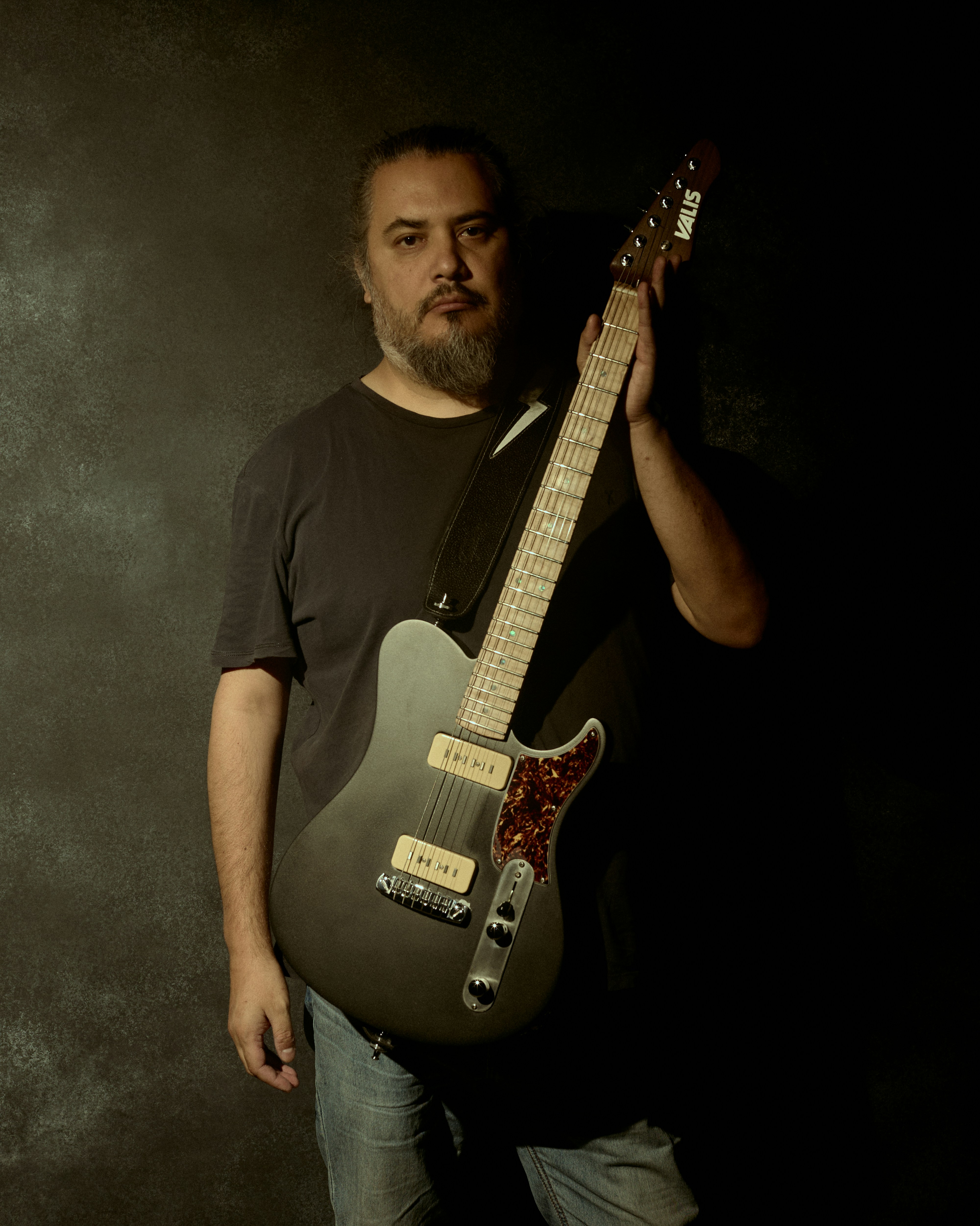 Man holding a dark electric guitar with a dark background