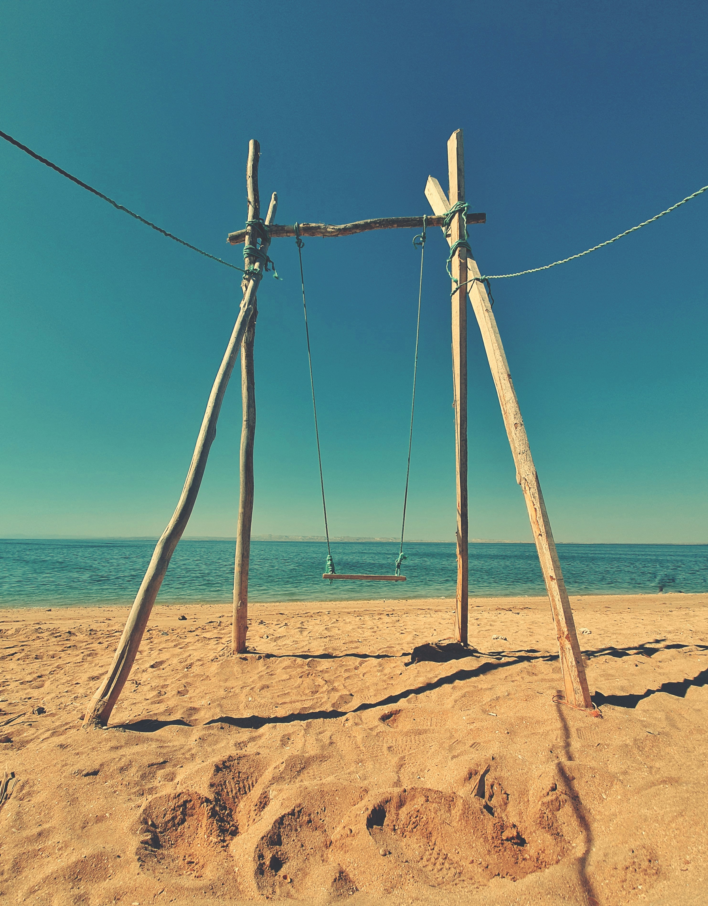 Wooden swing set on a sandy beach with ocean background