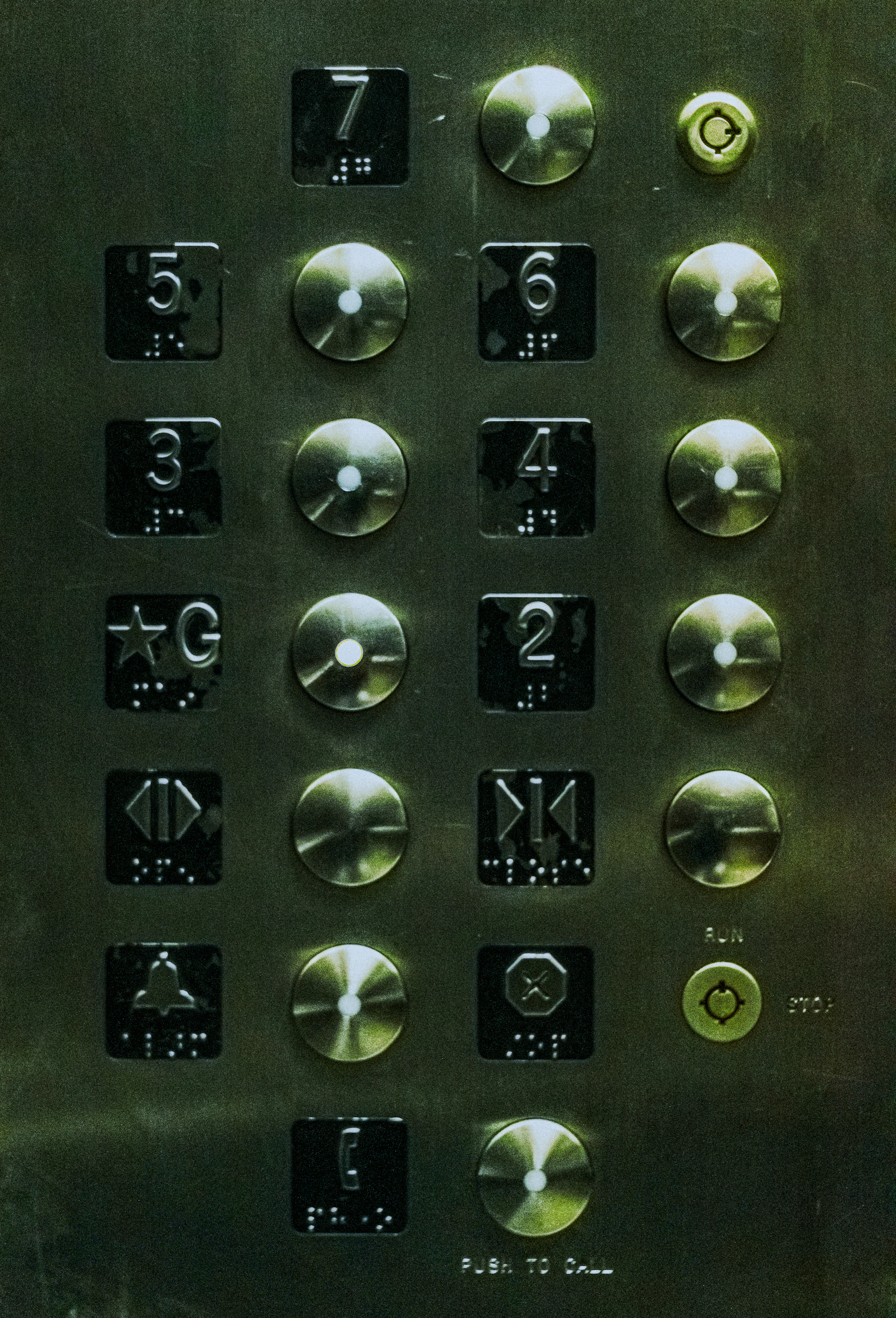 A brushed steel elevator panel, each floor number on a black plate with braille dots beneath it