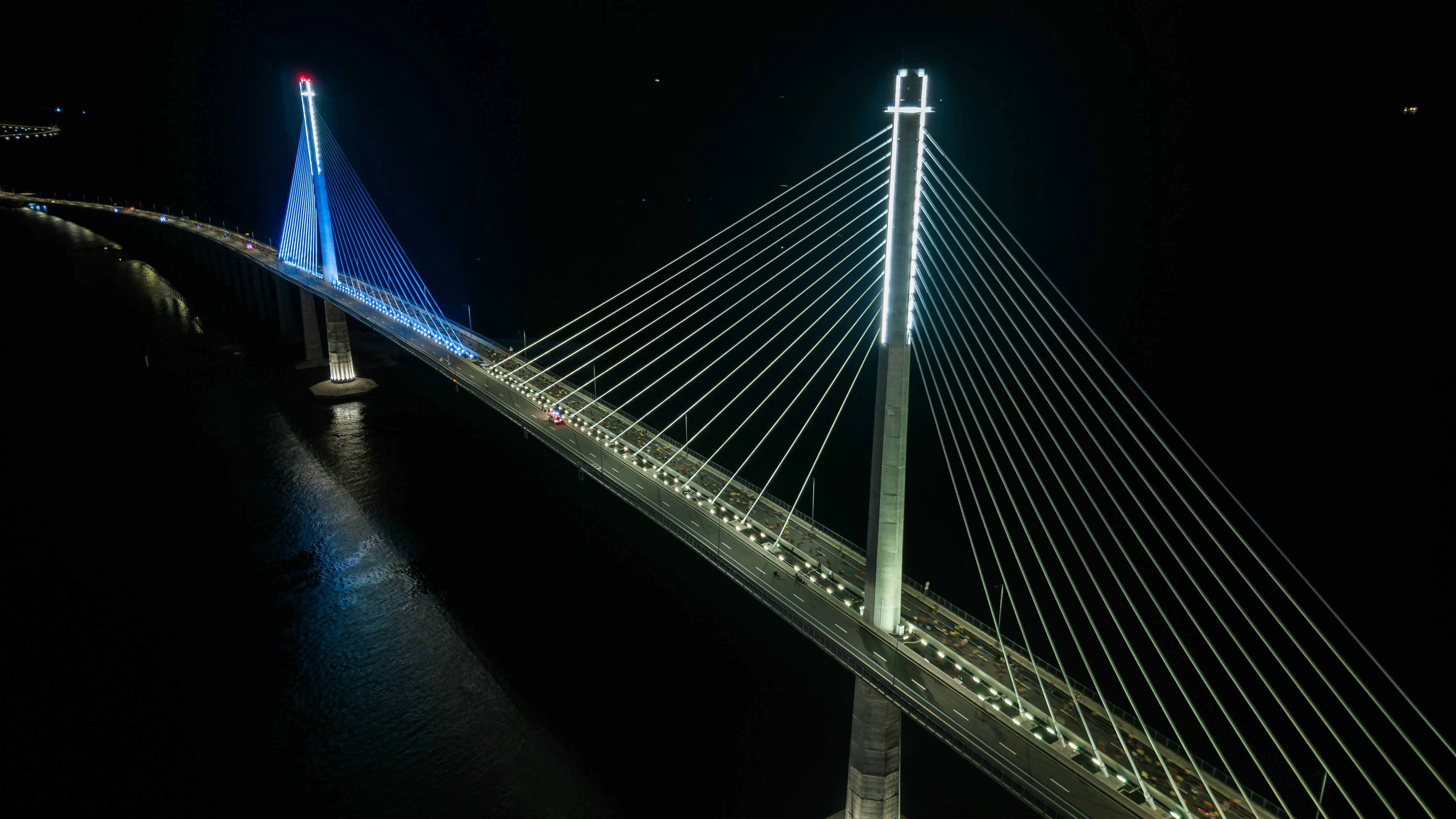 Illuminated cable-stayed bridge at night over dark water.