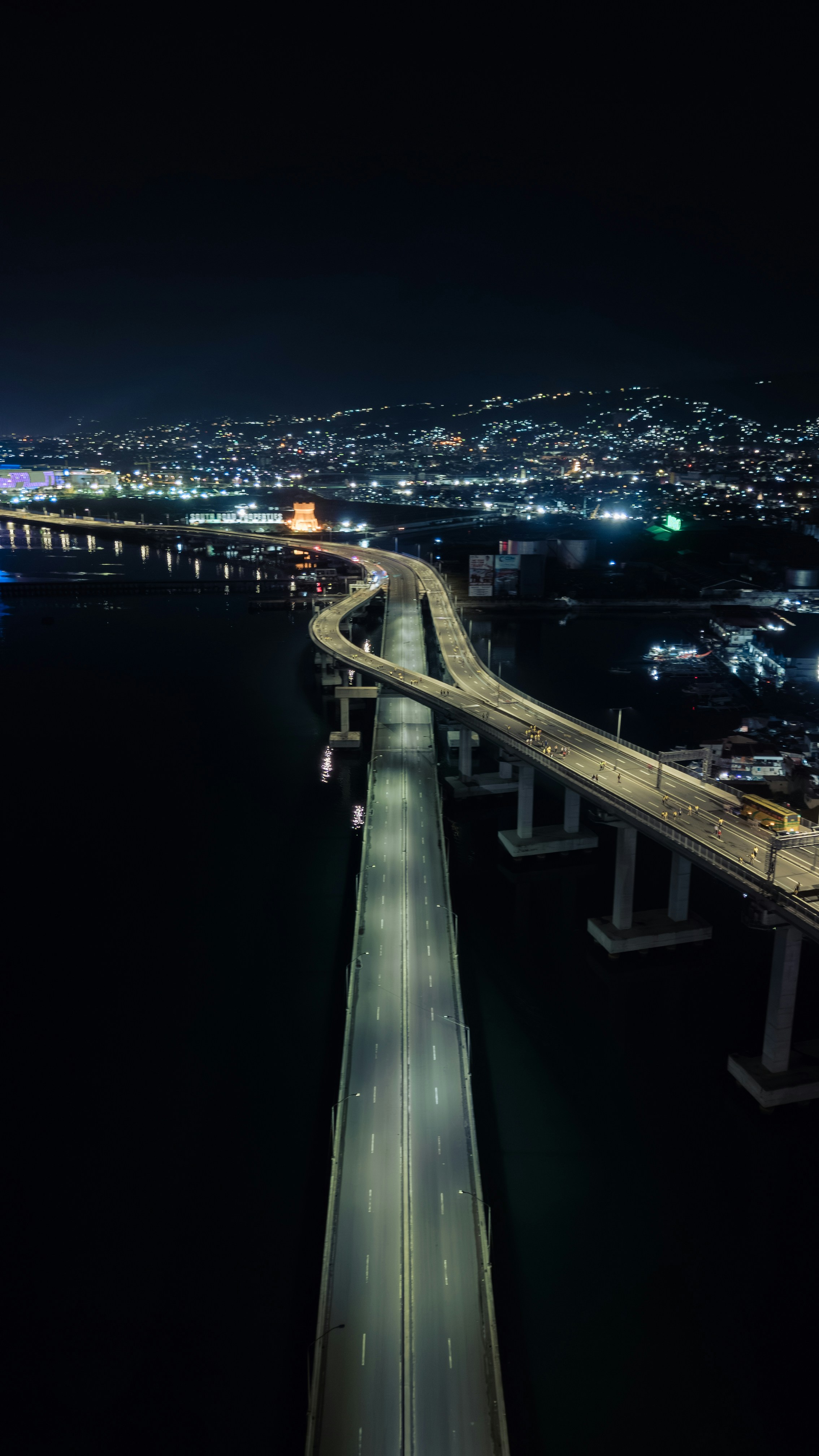 Illuminated bridge over dark water at night with city lights.