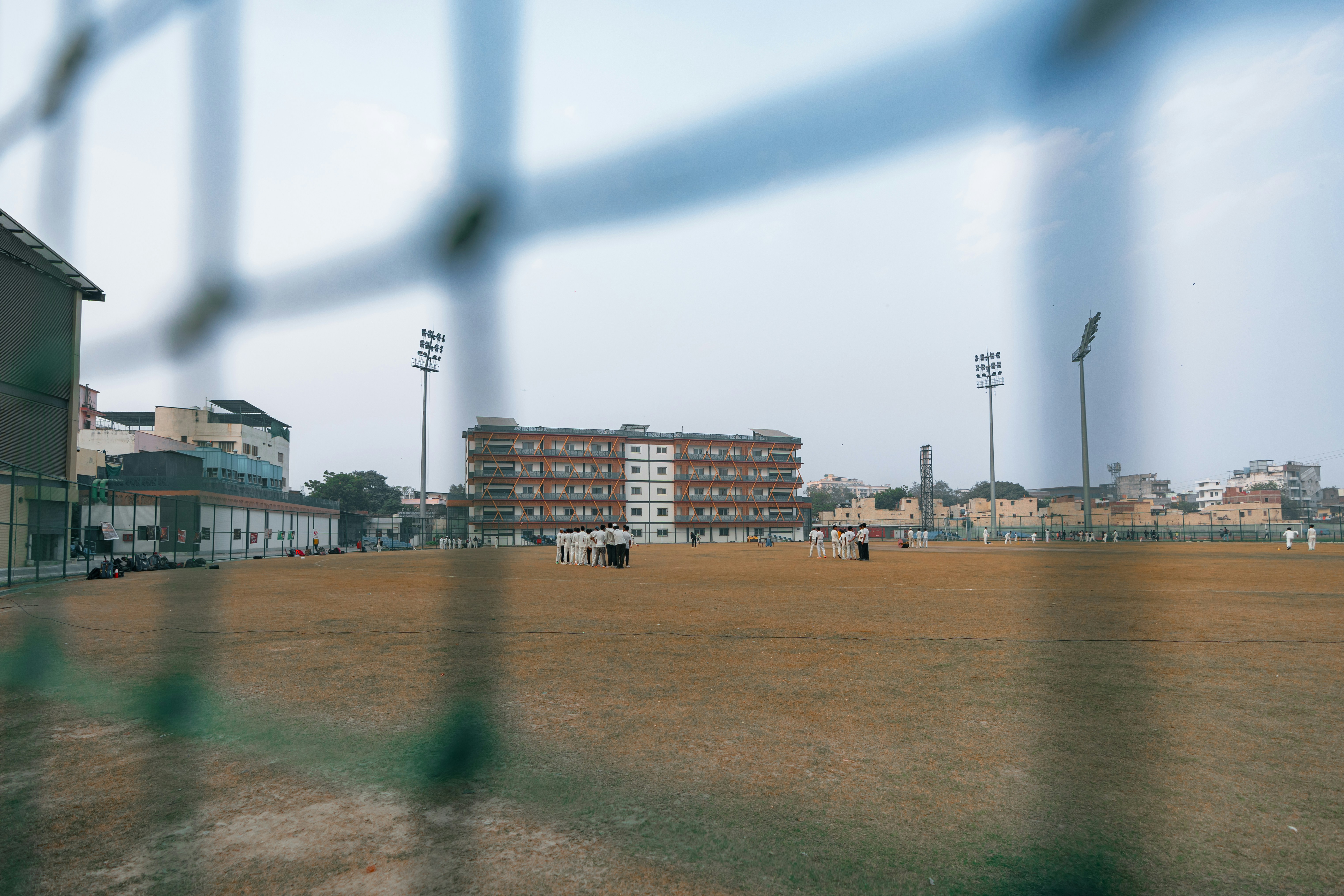 A sports field with buildings and lights in background.