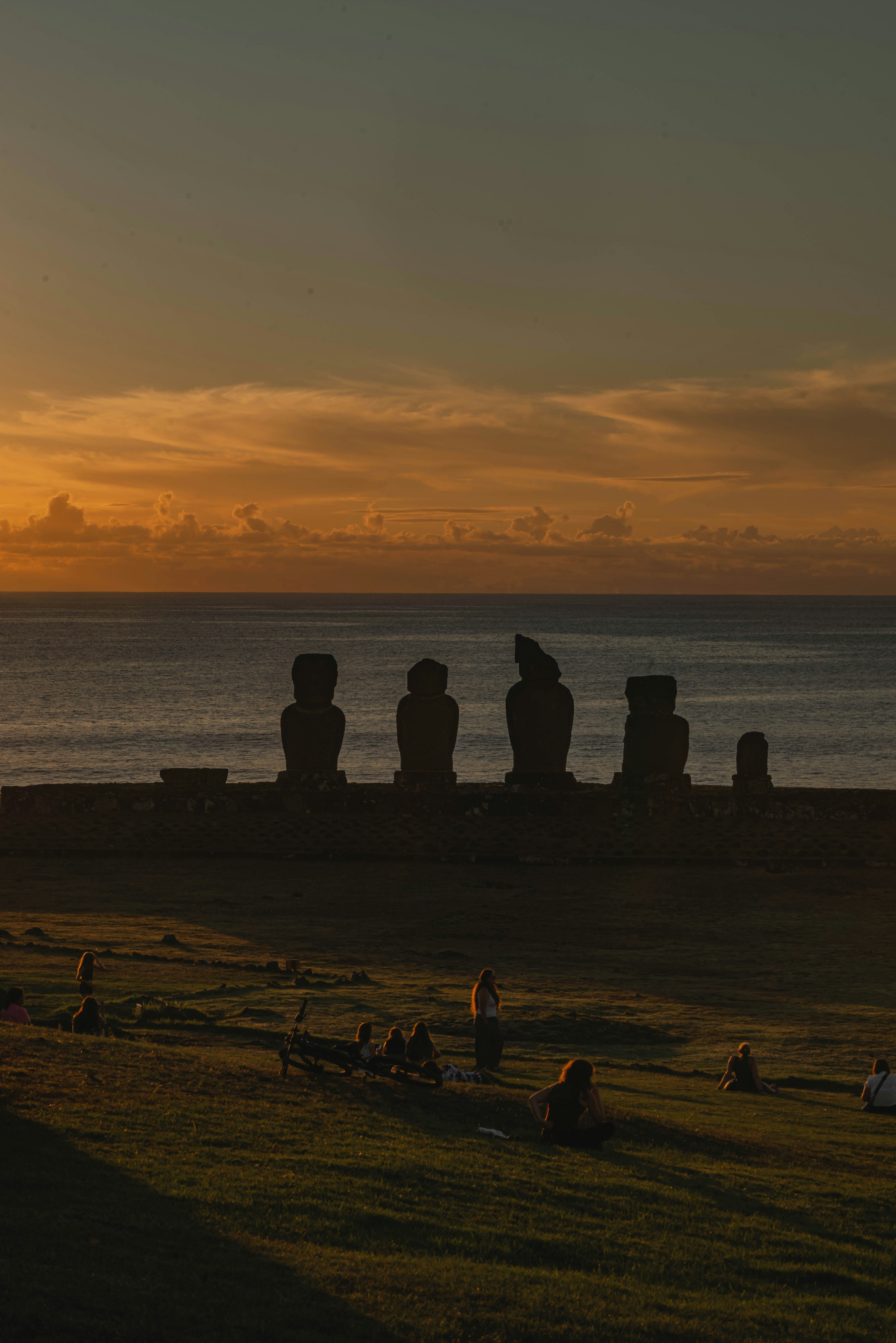 Moai statues silhouetted against a sunset over the ocean.