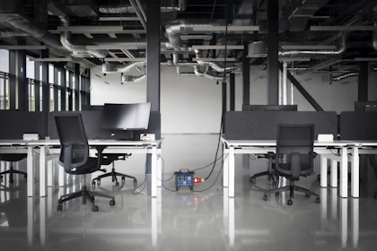 Modern office with desks, chairs, and exposed pipes.