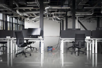 Modern office with desks, chairs, and exposed pipes.