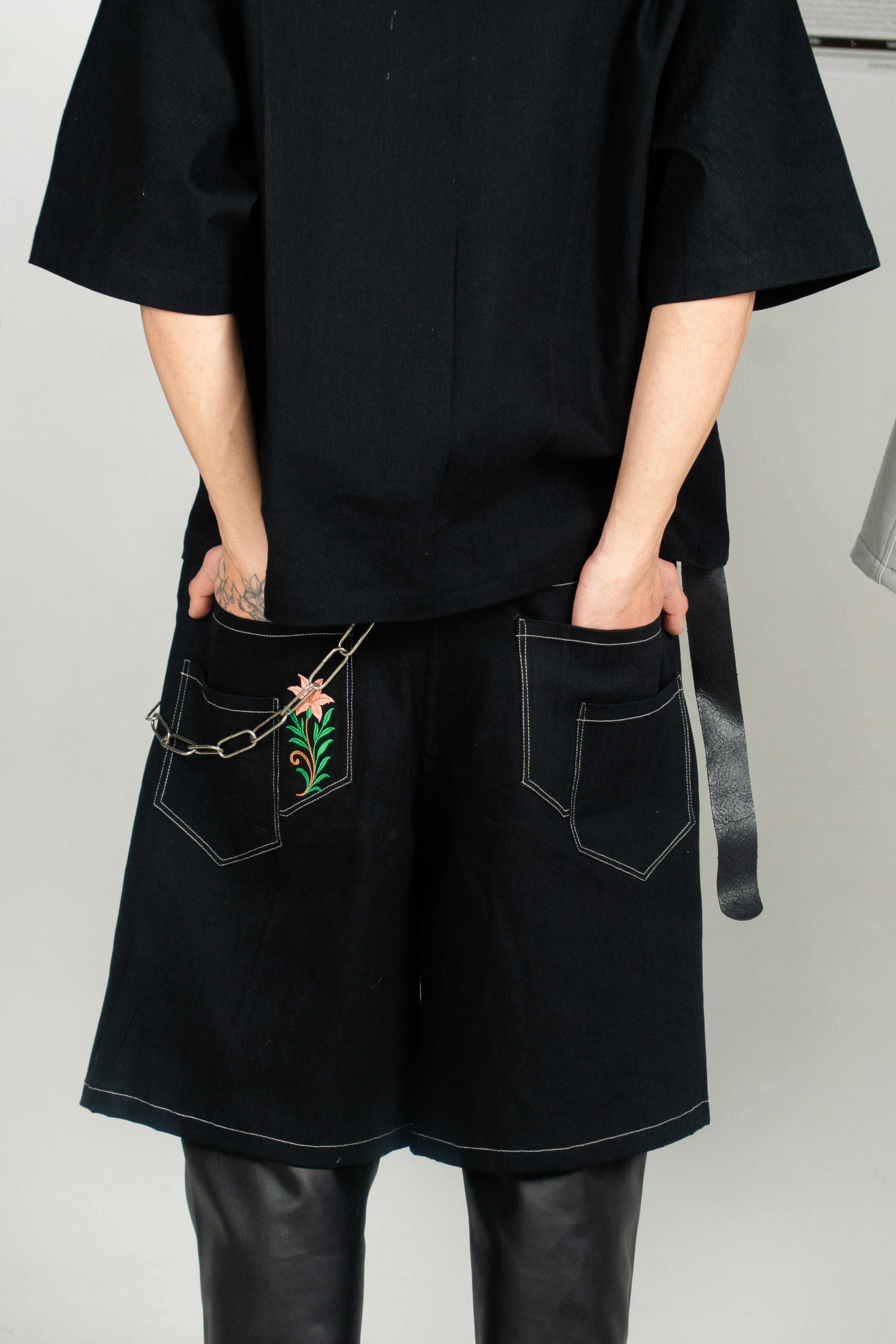 Person wearing black shorts with floral embroidery and chain.
