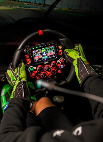 Hands in racing gloves grip a complex steering wheel.