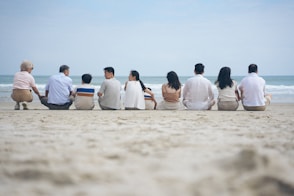 A family sits on a beach facing the ocean.