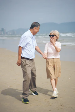 Elderly couple walking hand-in-hand on a sandy beach.