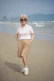 Elderly woman standing on a beach with hands in pockets.