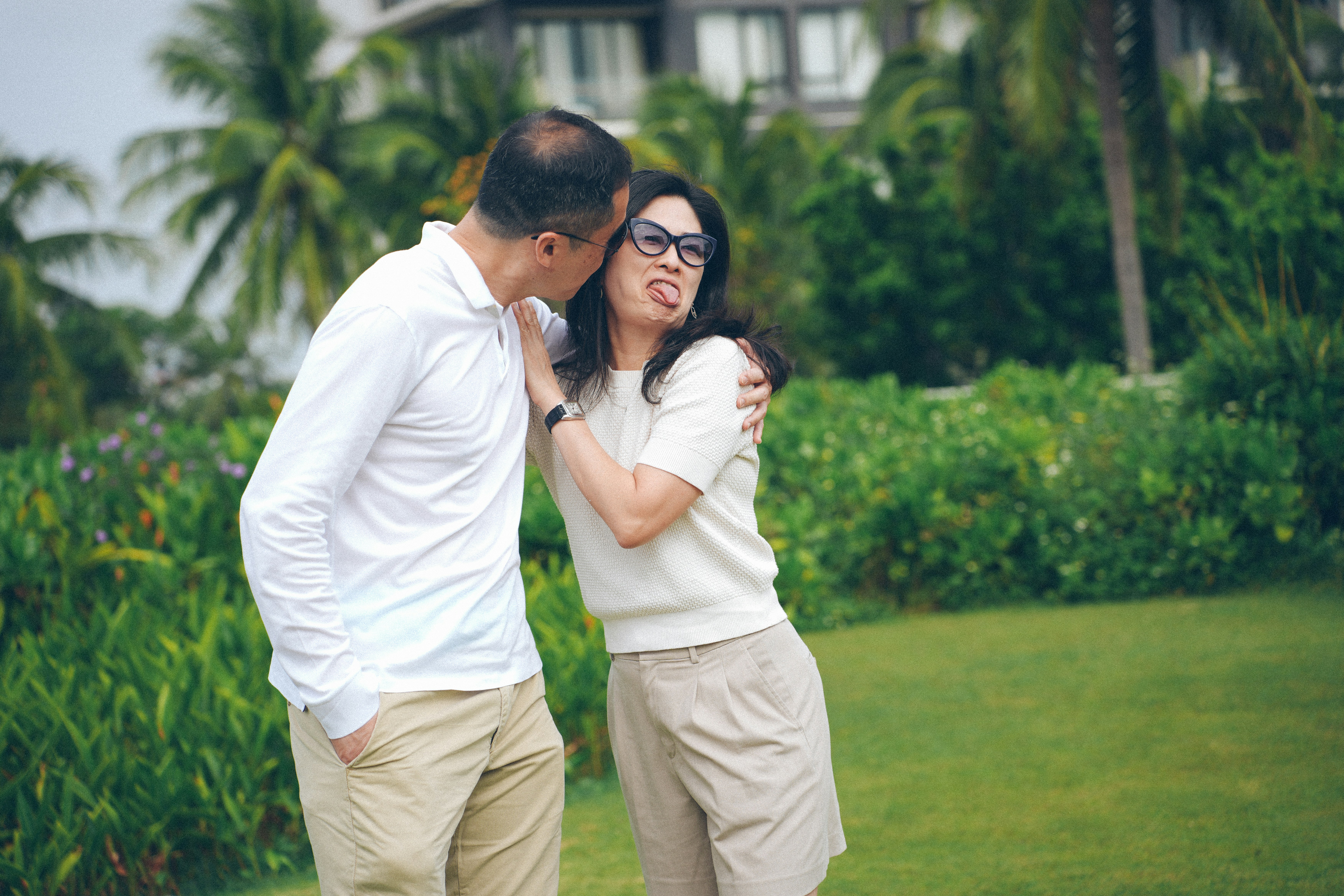 Couple playfully posing outdoors with palm trees and greenery.