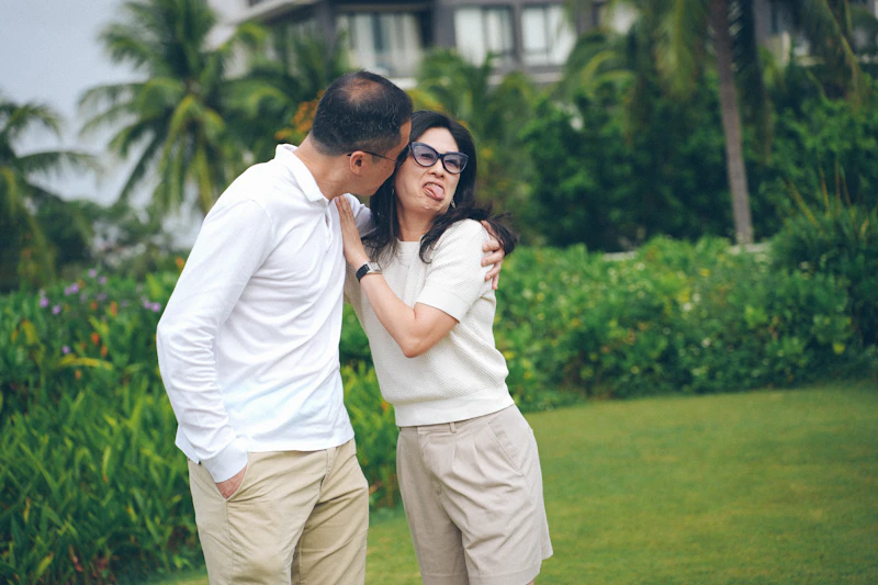 Couple playfully posing outdoors with palm trees and greenery.
