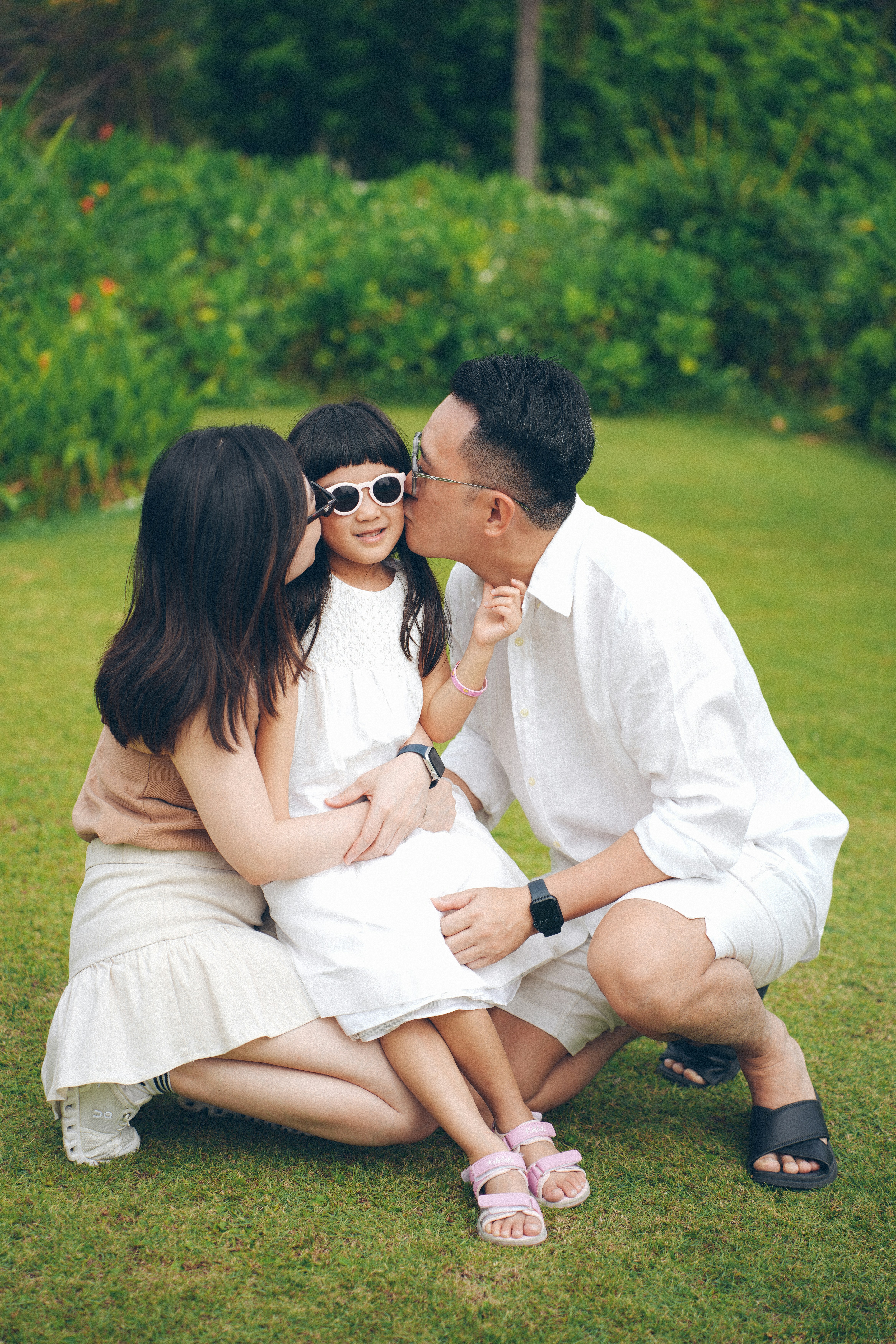 Eltern, die ihre Tochter auf einem grasbewachsenen Rasen küssen.
